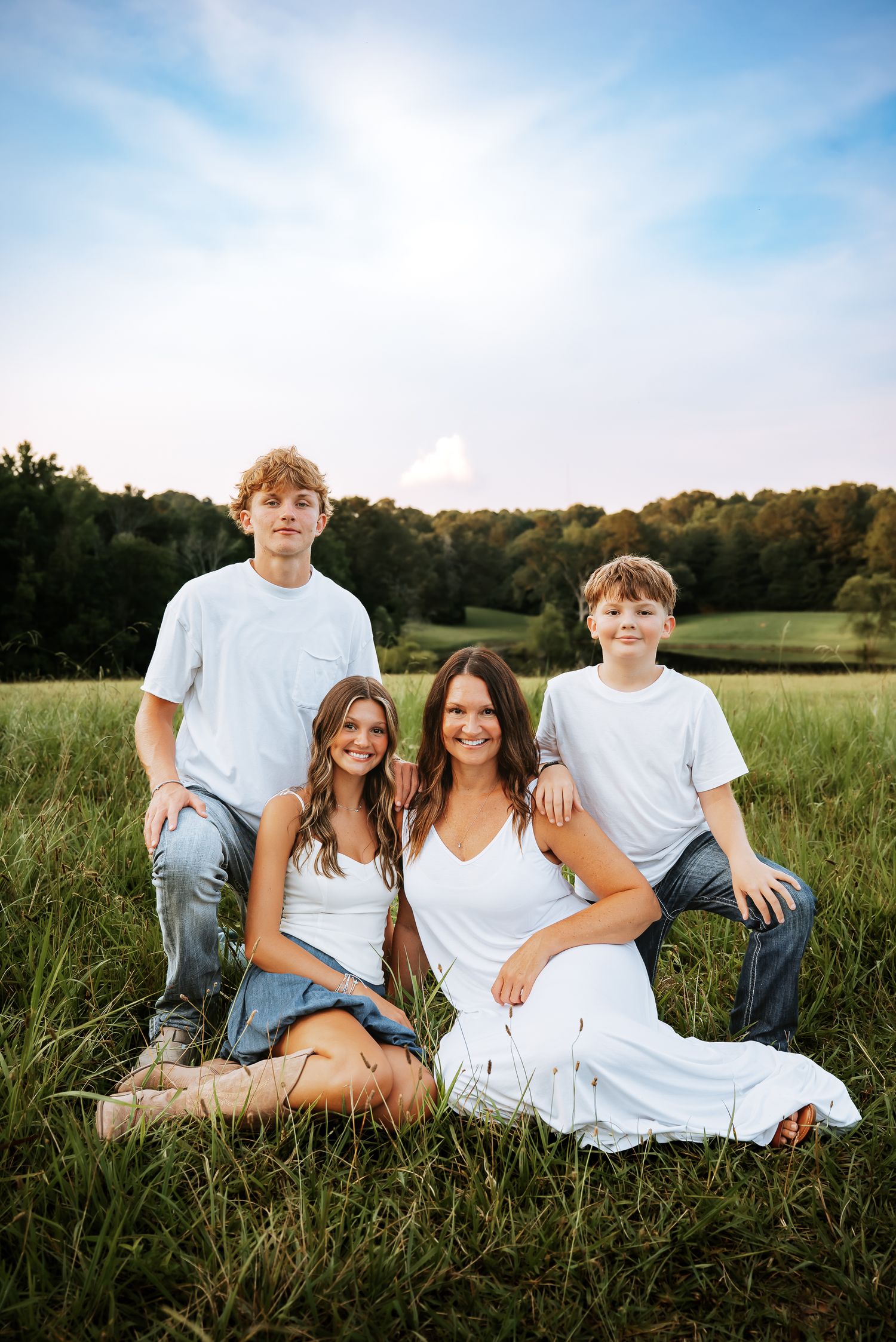 Family portrait session in a lush green field with blue sky backdrop.