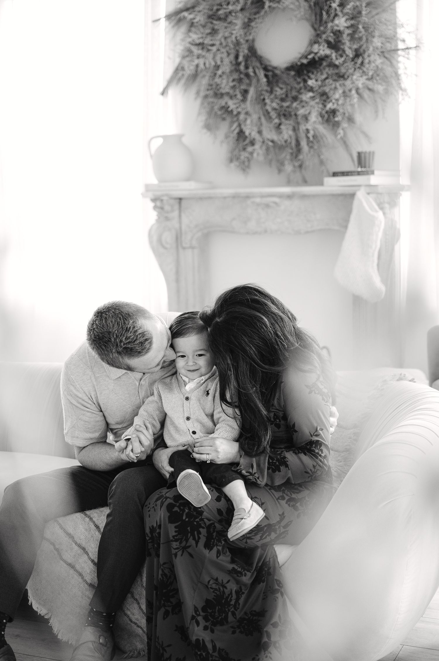 Family shares intimate moment on couch beneath holiday wreath.