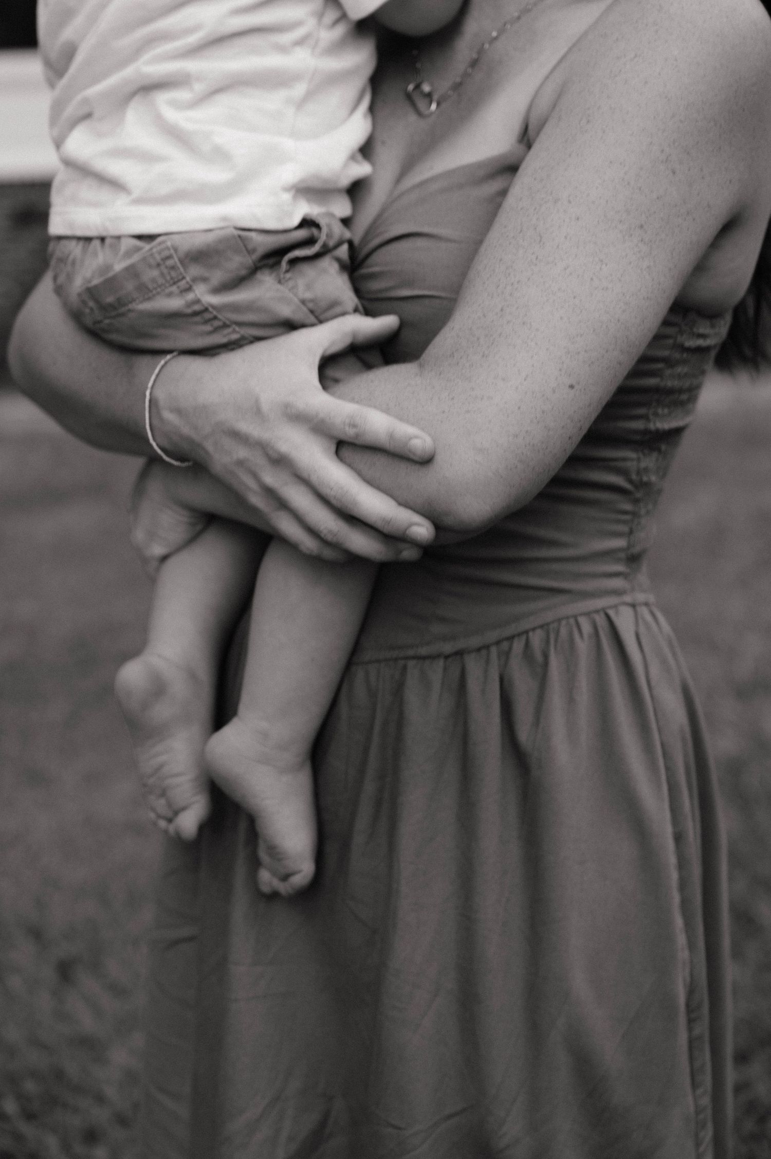 Black and white photo of a mother in a sundress tenderly holding a young baby in her arms outdoors.