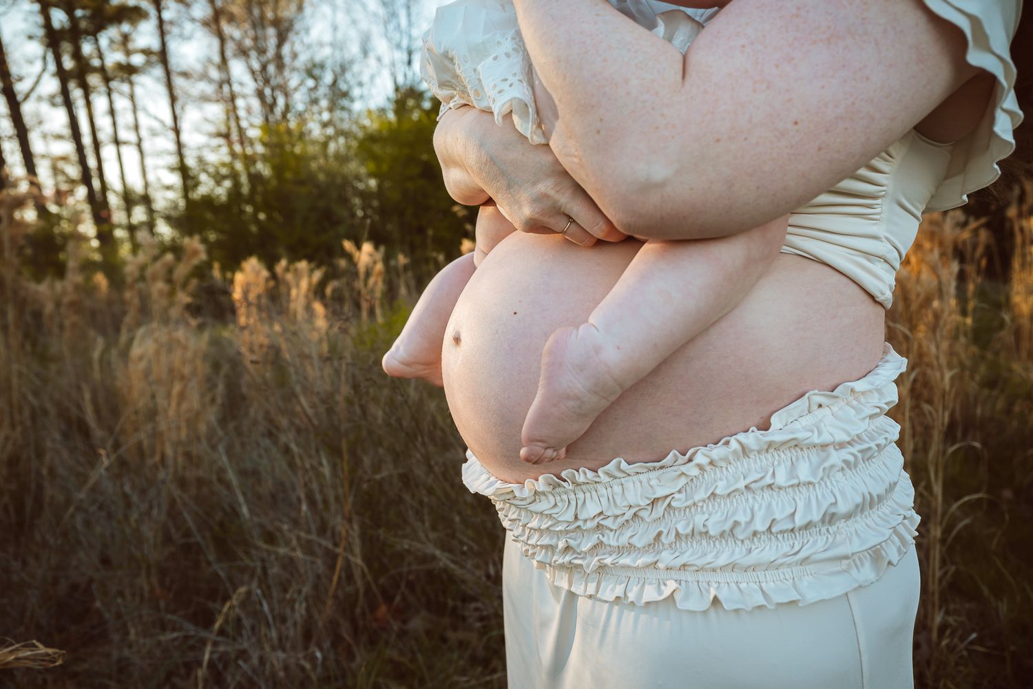 Close up maternity photo showing hands cradling pregnant belly in white dress.