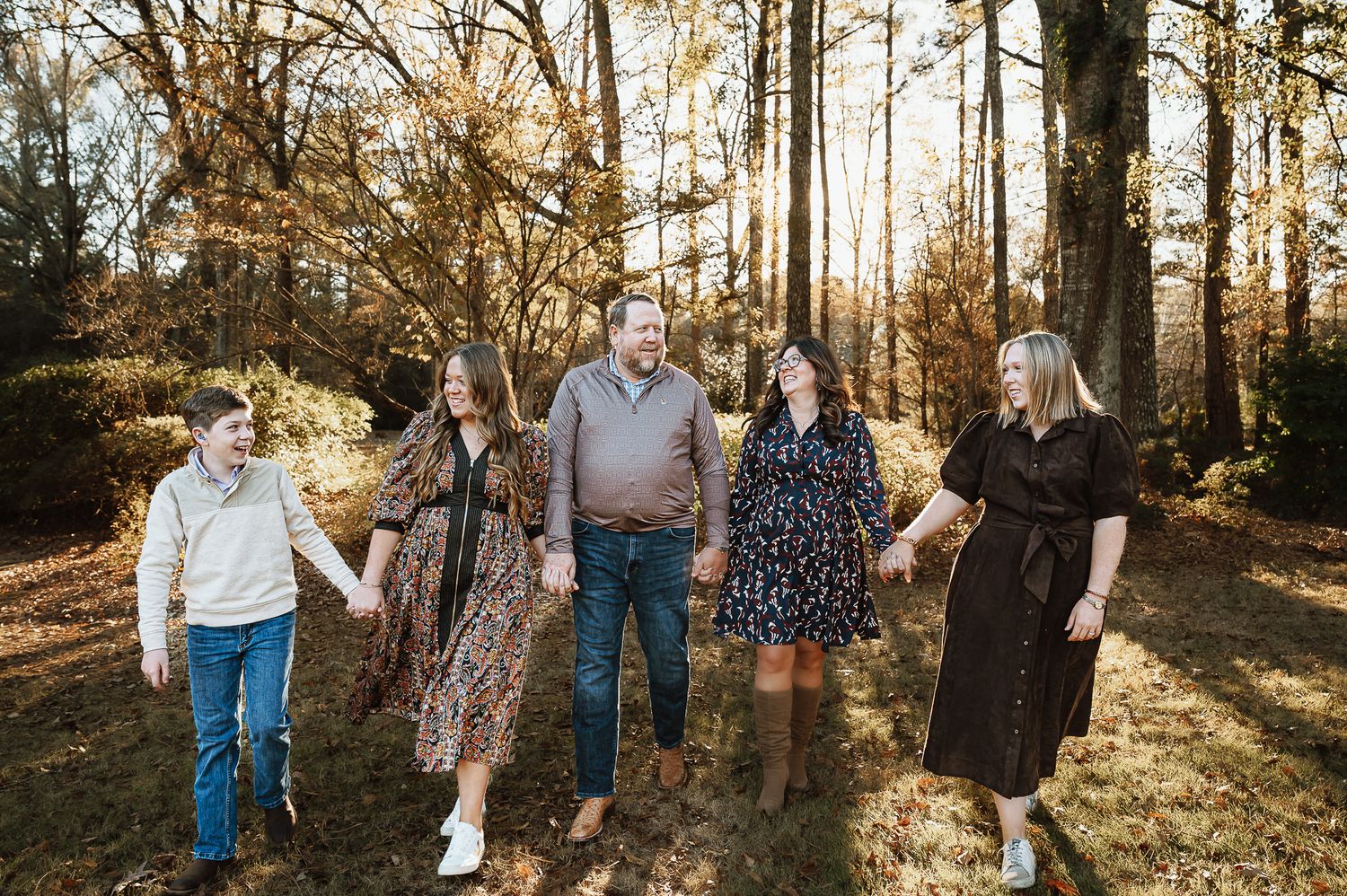Family walking together through a sunlit wooded area during golden hour.
