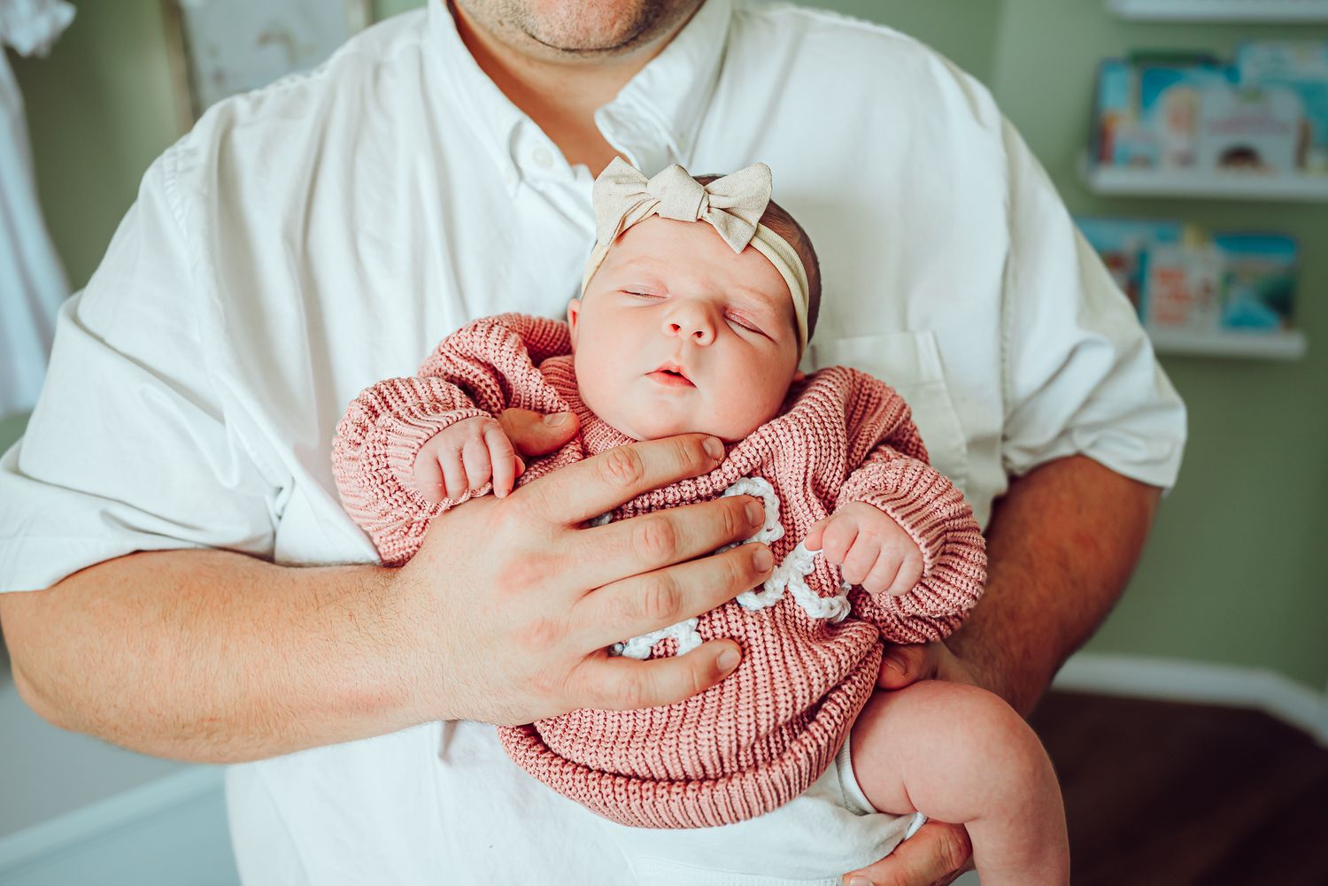 A sleeping baby wearing pink with a white bow being cradled gently.