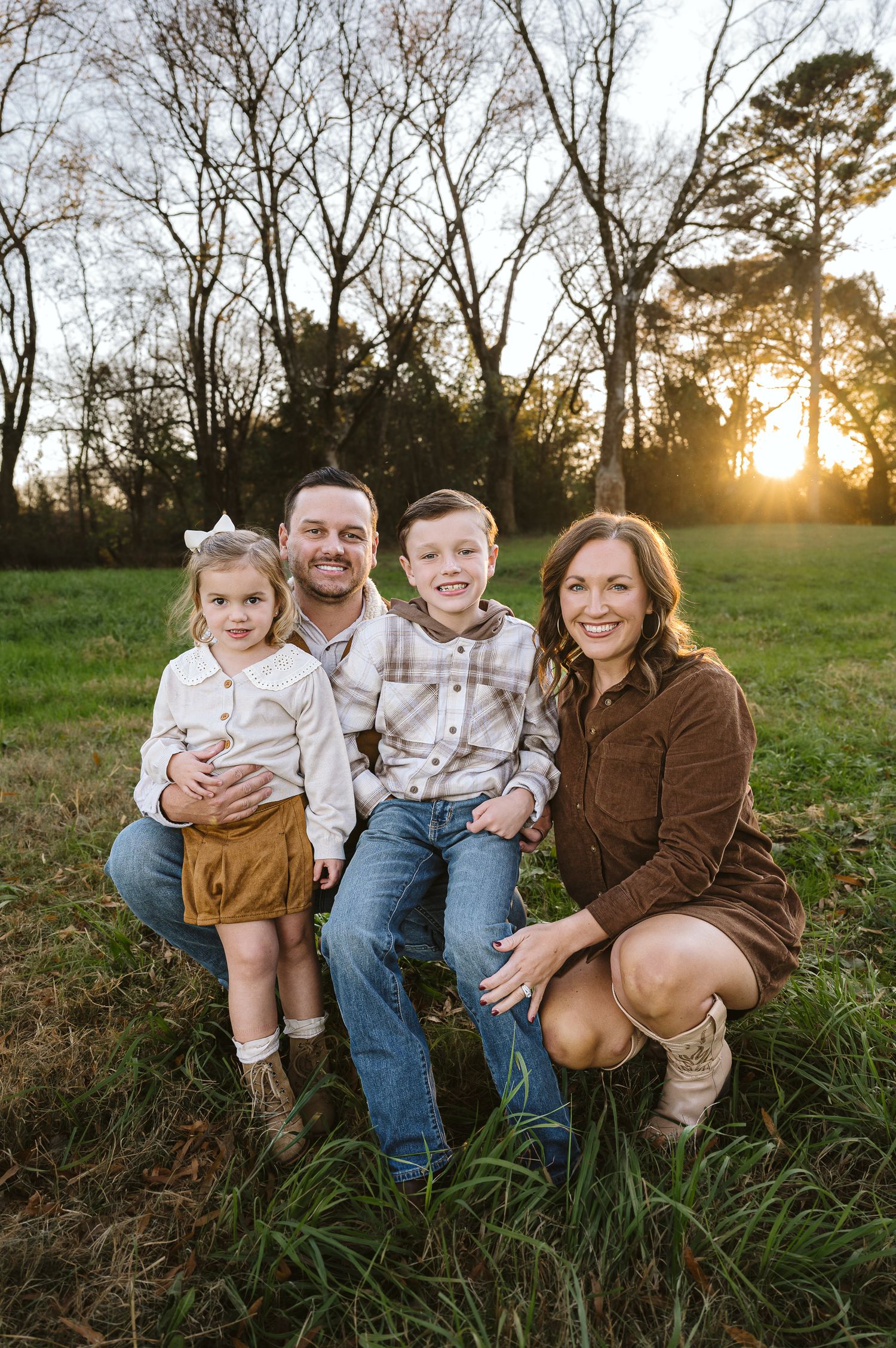 Family sitting together in tall grass during sunset for outdoor portraits.