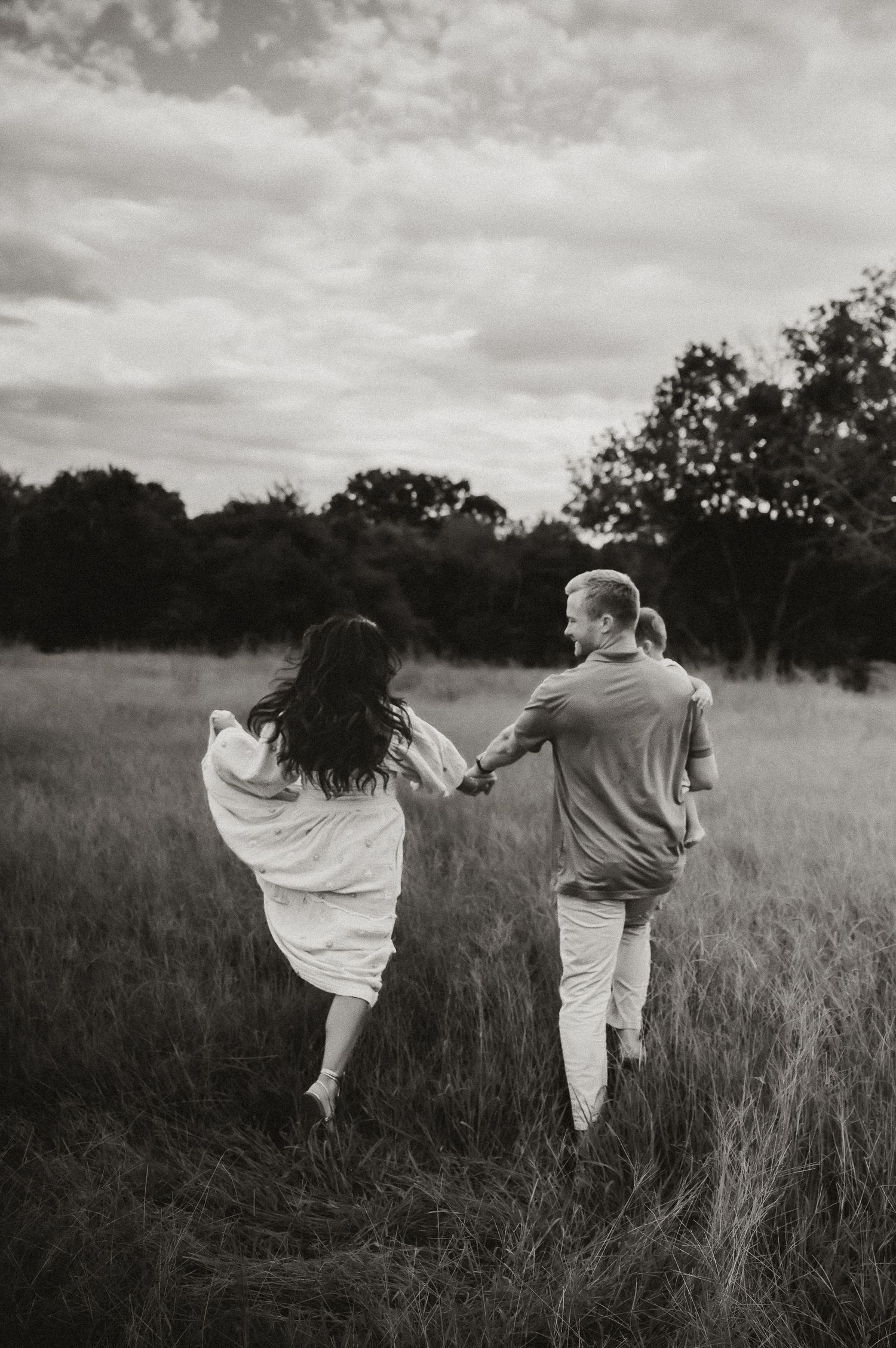 Black and white photos of a couple dancing playfully in a field.