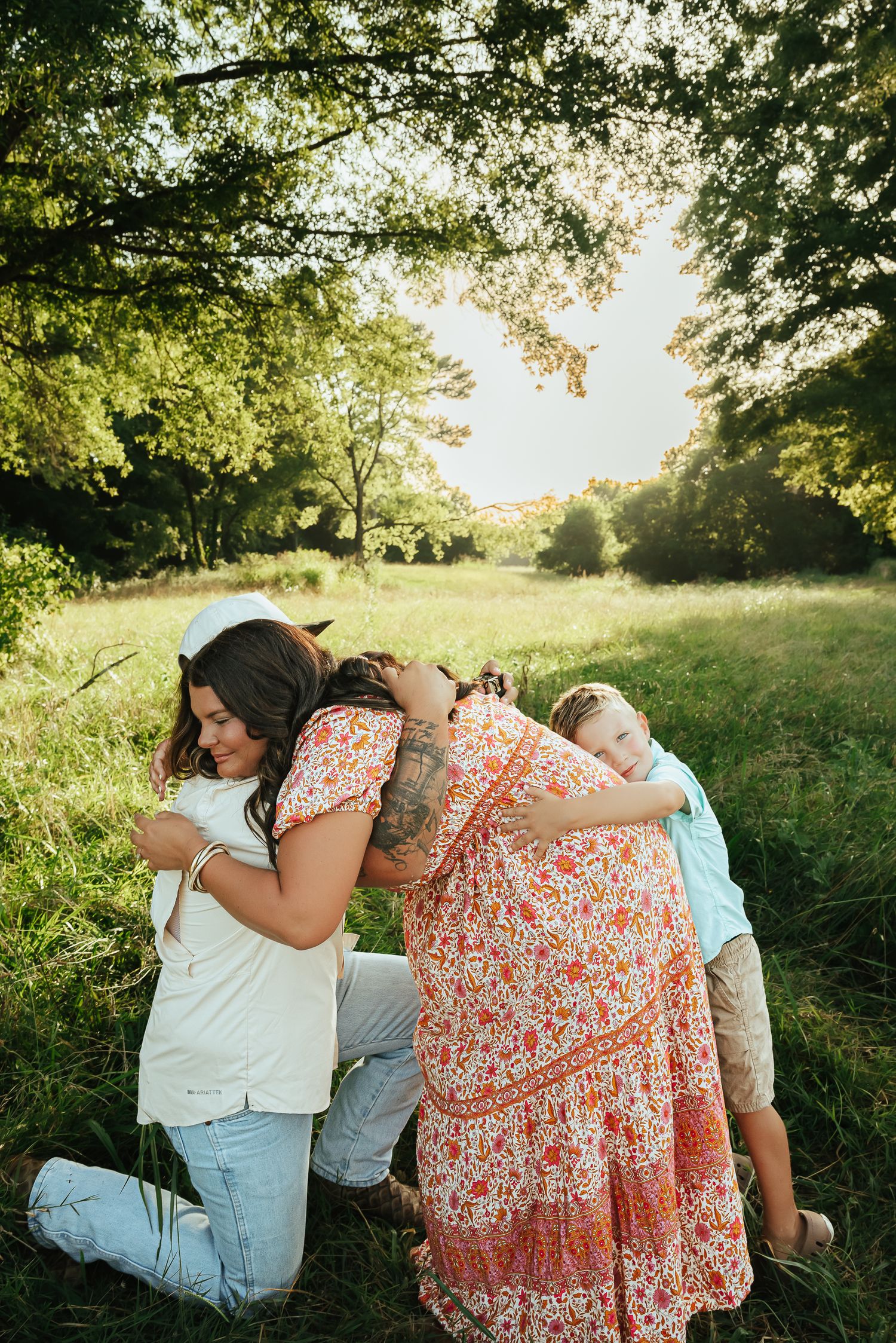 Romantic couple in casual attire embracing in sunny meadow with trees.