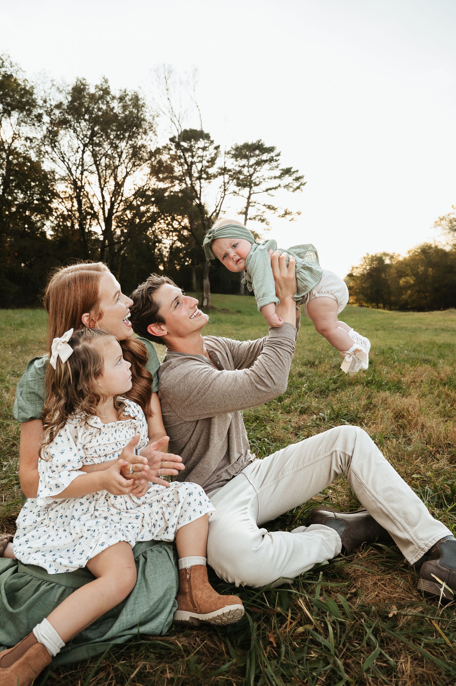 Family enjoys playful moment together in sunlit field during portrait session.