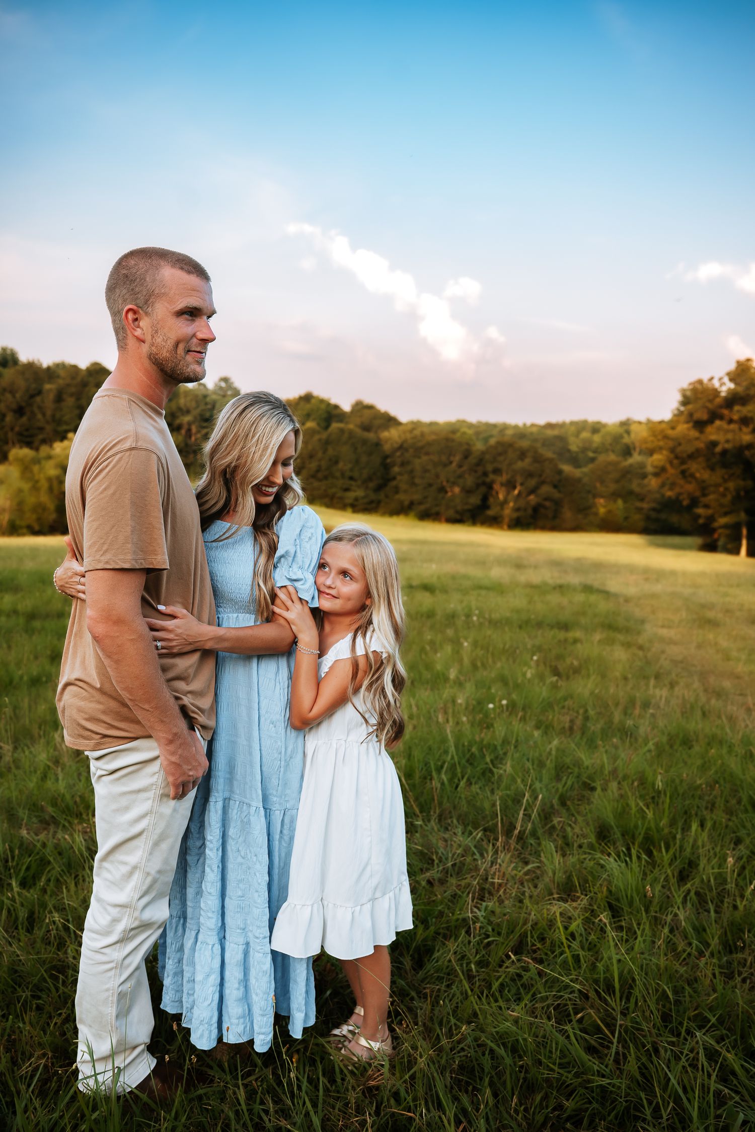 Family embracing in a summer field wearing light colored clothing at sunset.