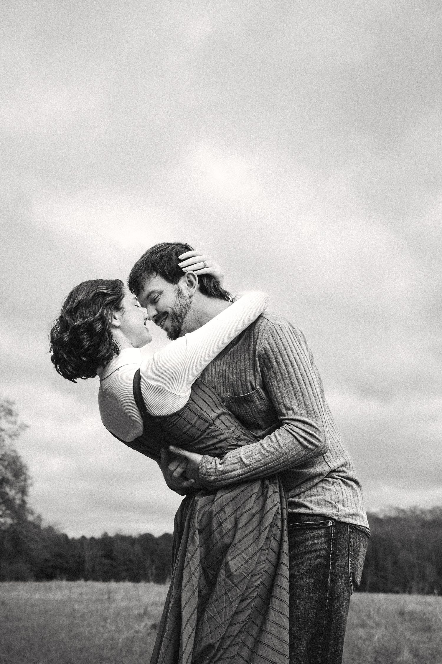 Romantic black and white portrait of couple embracing in field.
