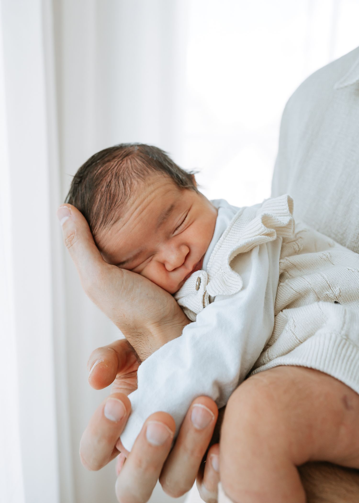 A peaceful newborn baby sleeps soundly while being cradled in gentle hands.