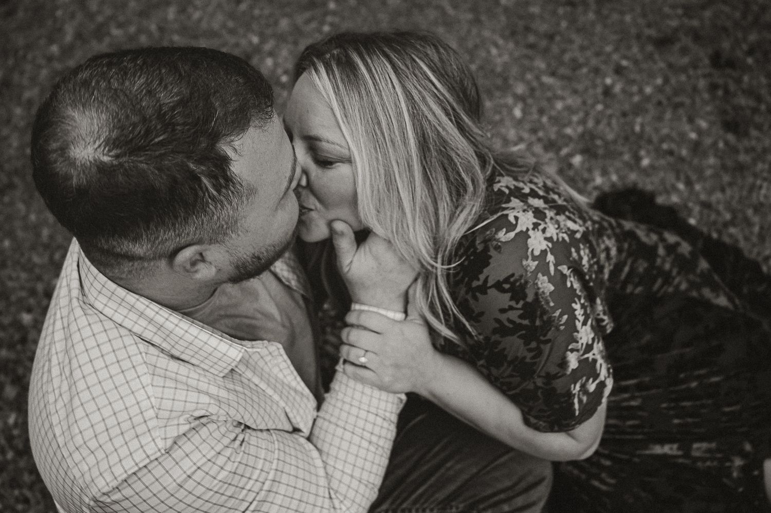 A romantic black and white photo of a couple sharing an intimate moment while lying in the grass.