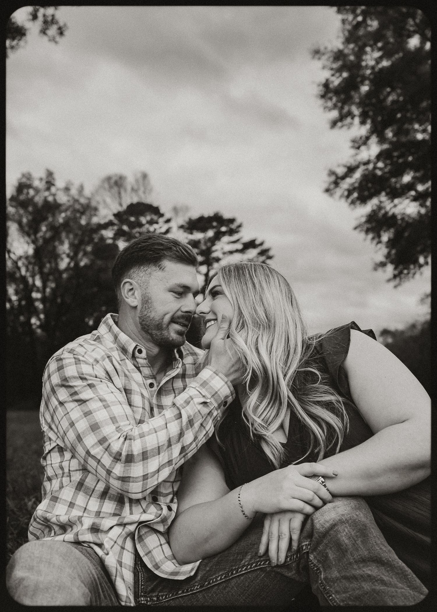 A black and white portrait of a couple sharing a playful intimate moment outdoors.