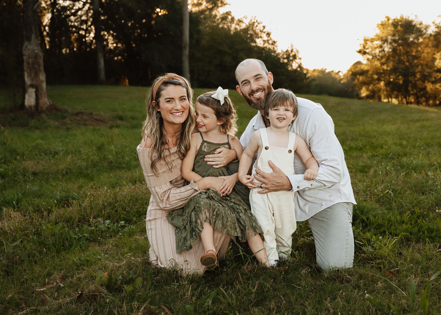 Family of four poses together in grassy field during golden hour portrait session.