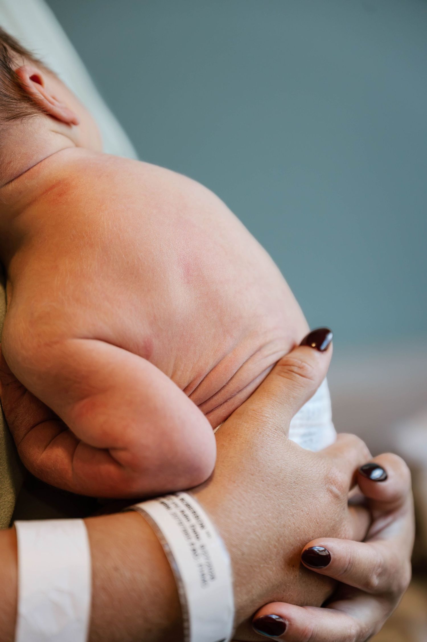 A newborn baby cradled in a mother's arm, with a hospital wristband visible on her wrist.