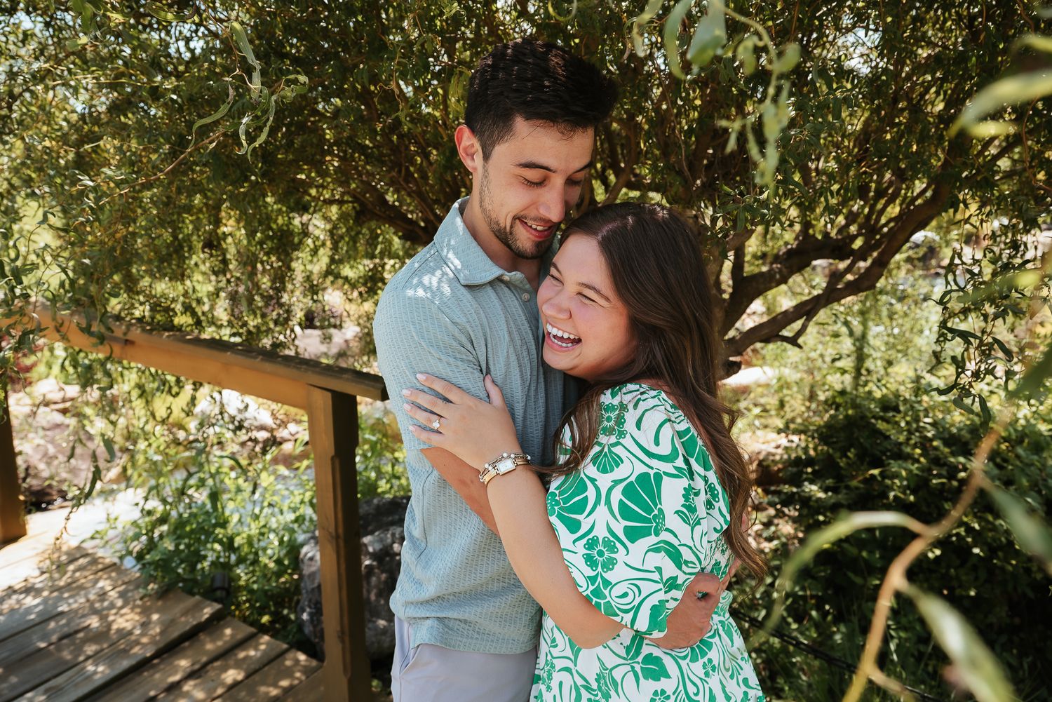 Couple sharing tender moments under green leafy trees in natural lighting.