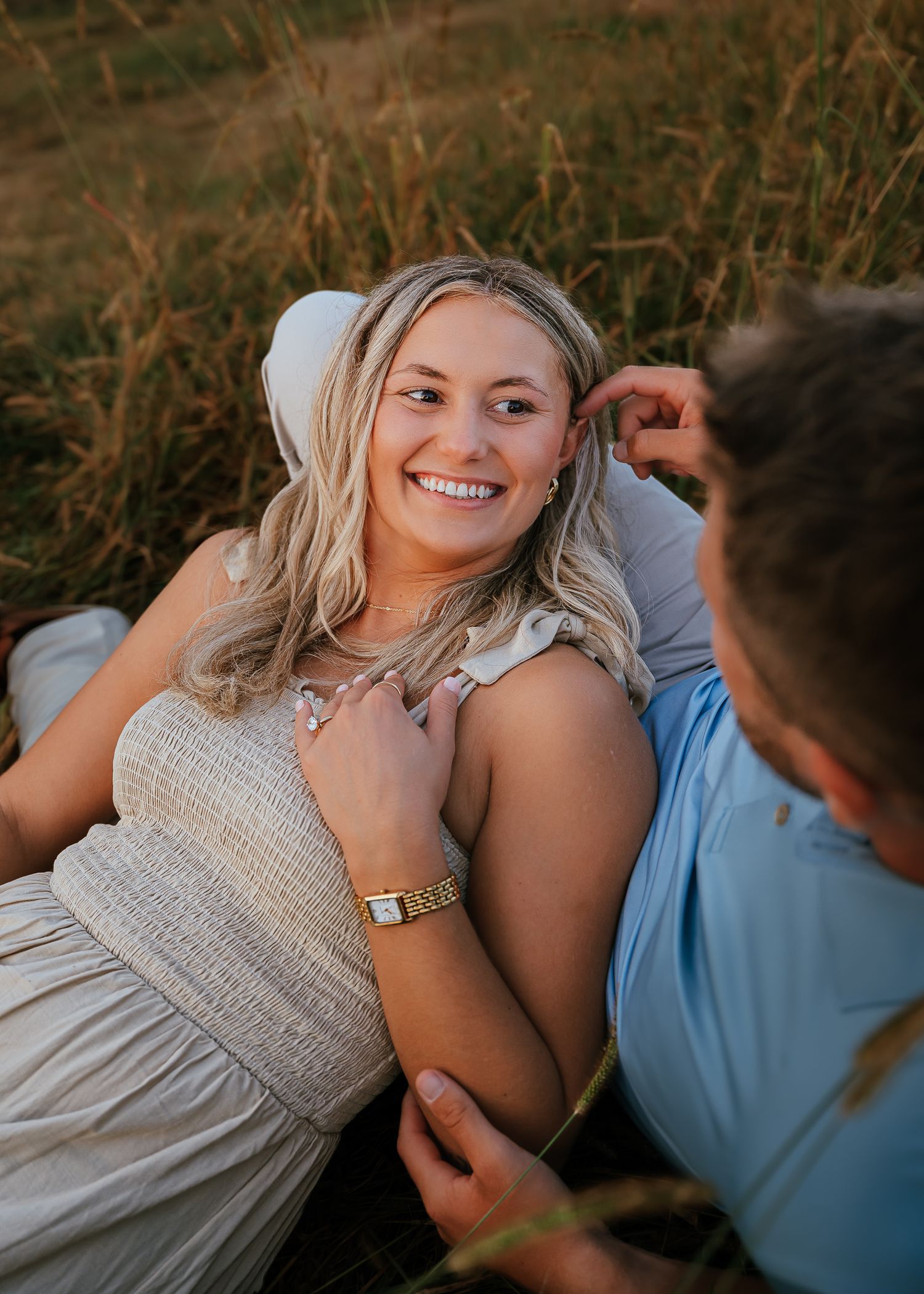Couple lying in tall grass during golden hour outdoor photo session.