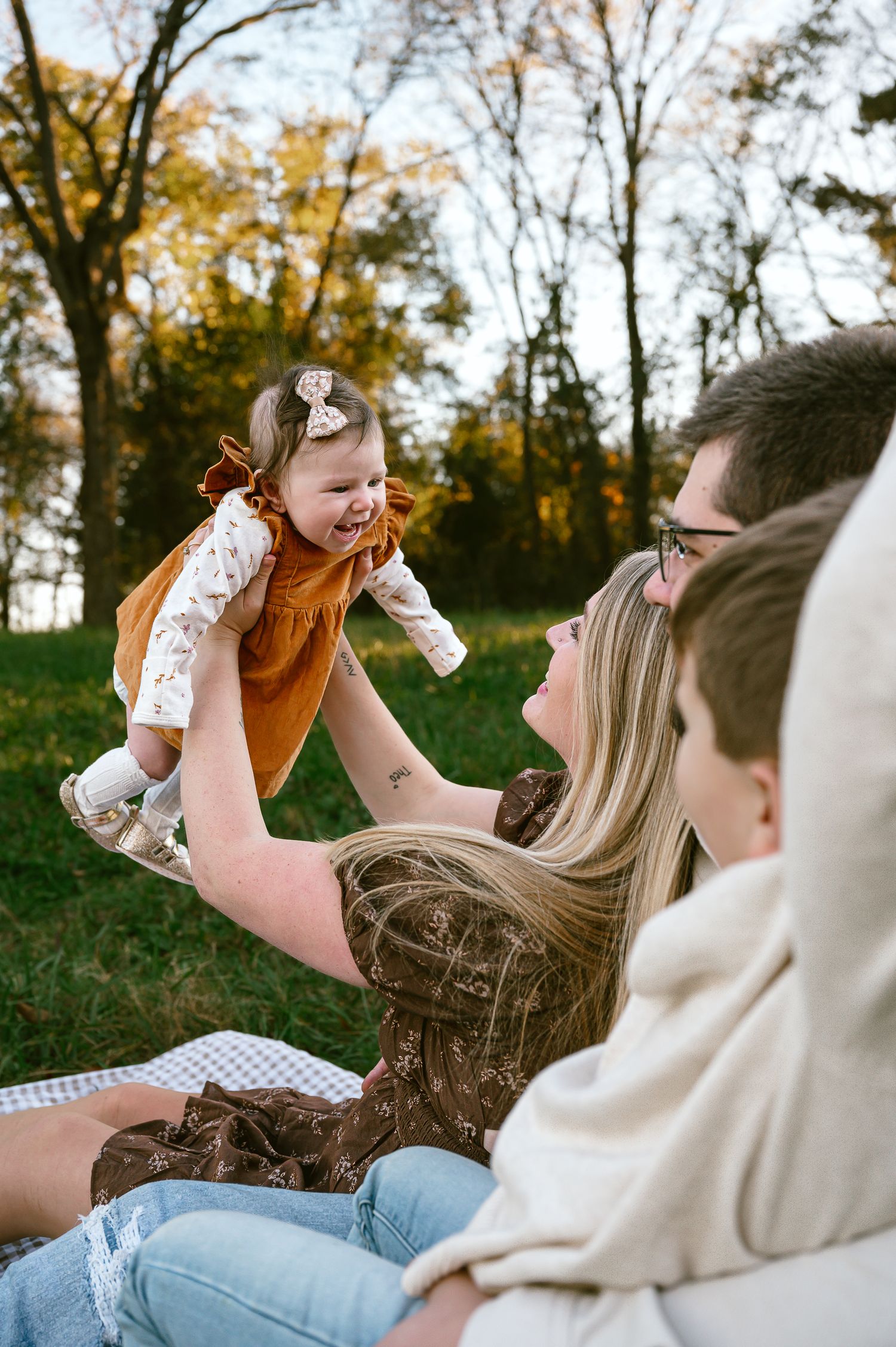 Playful family moments captured on a blanket outdoors during golden hour.
