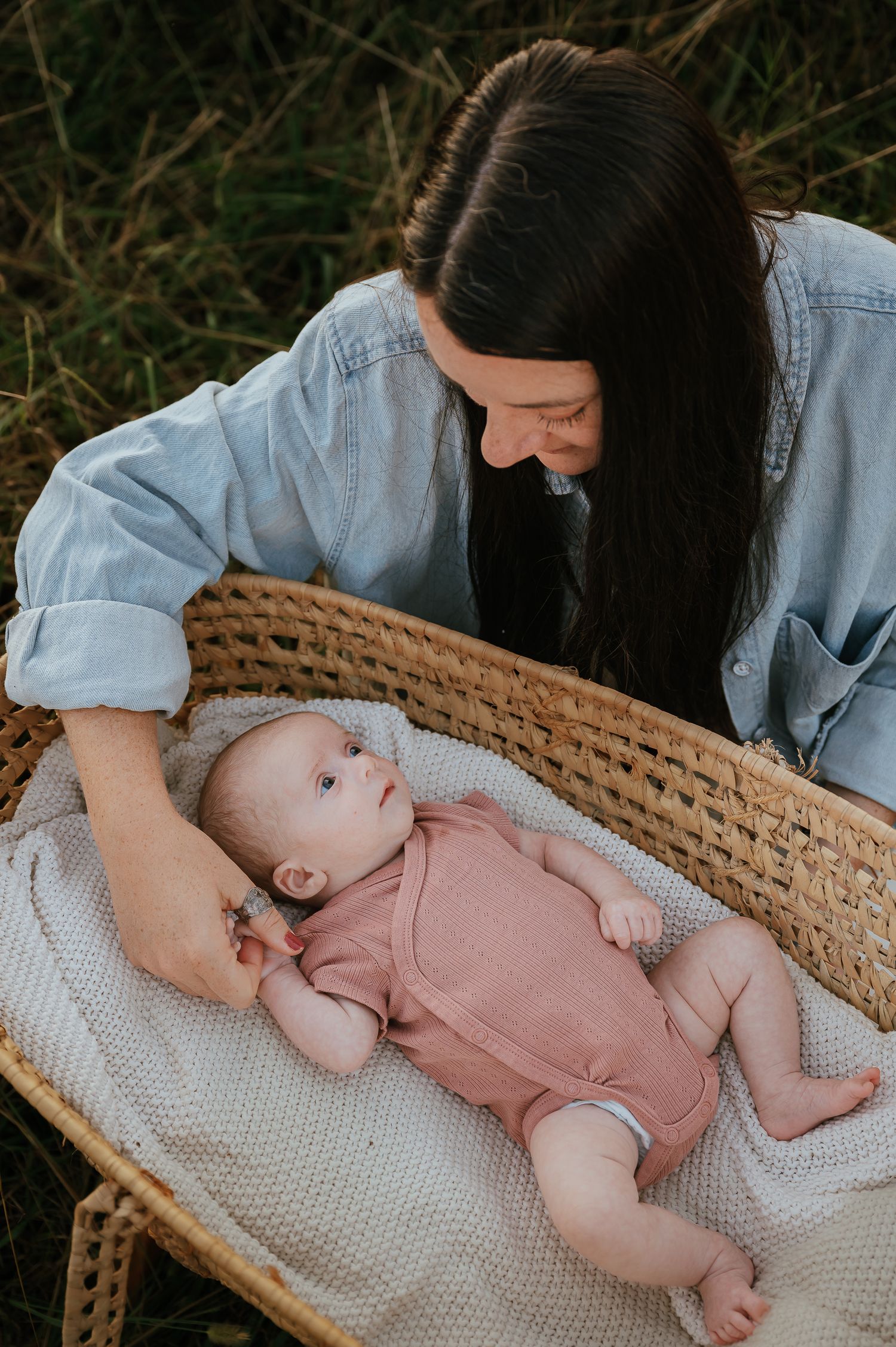 Baby in pink romper resting in woven basket with white blanket.