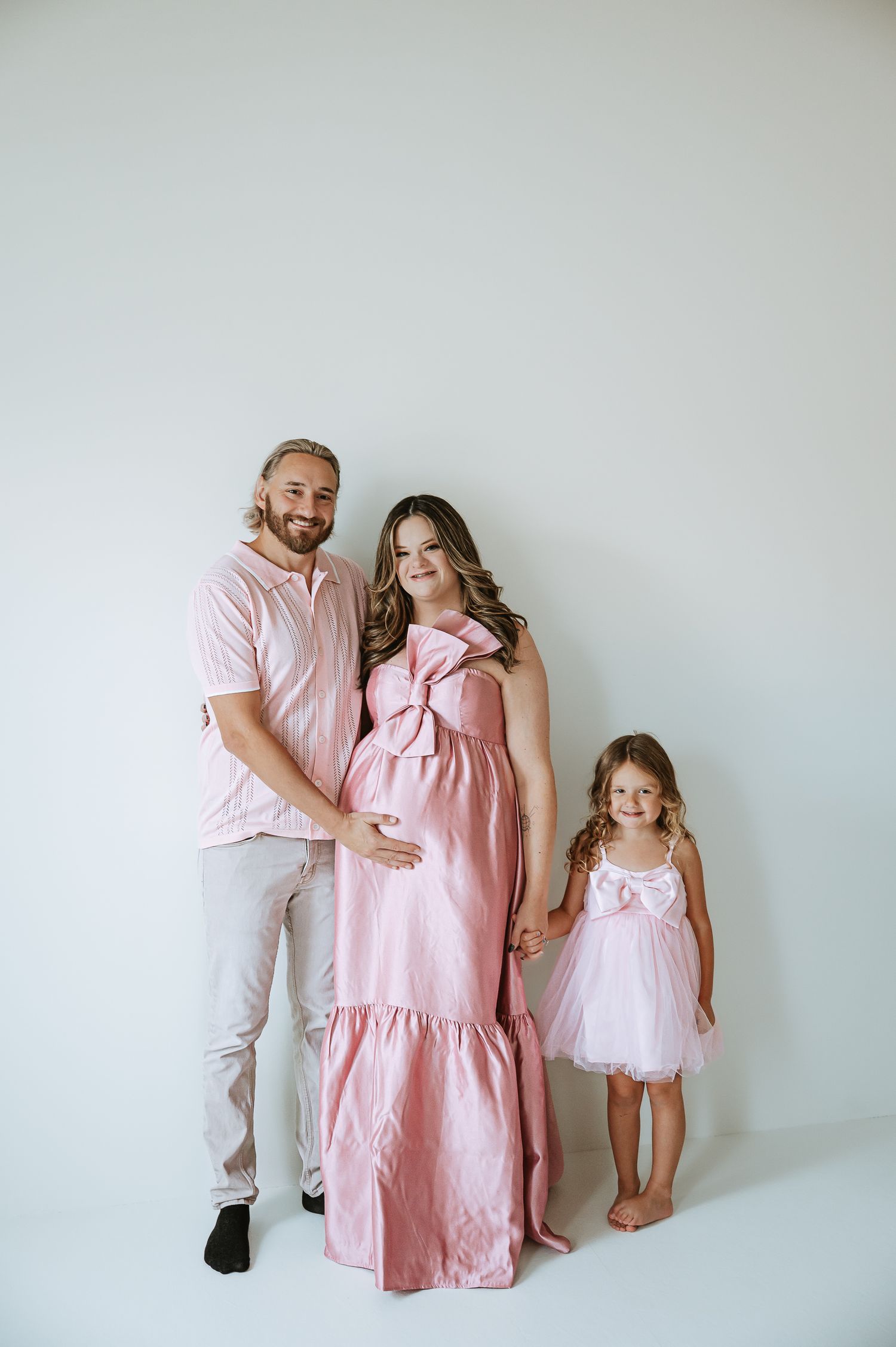 Family photo series in pink and white outfits against a minimalist white backdrop.