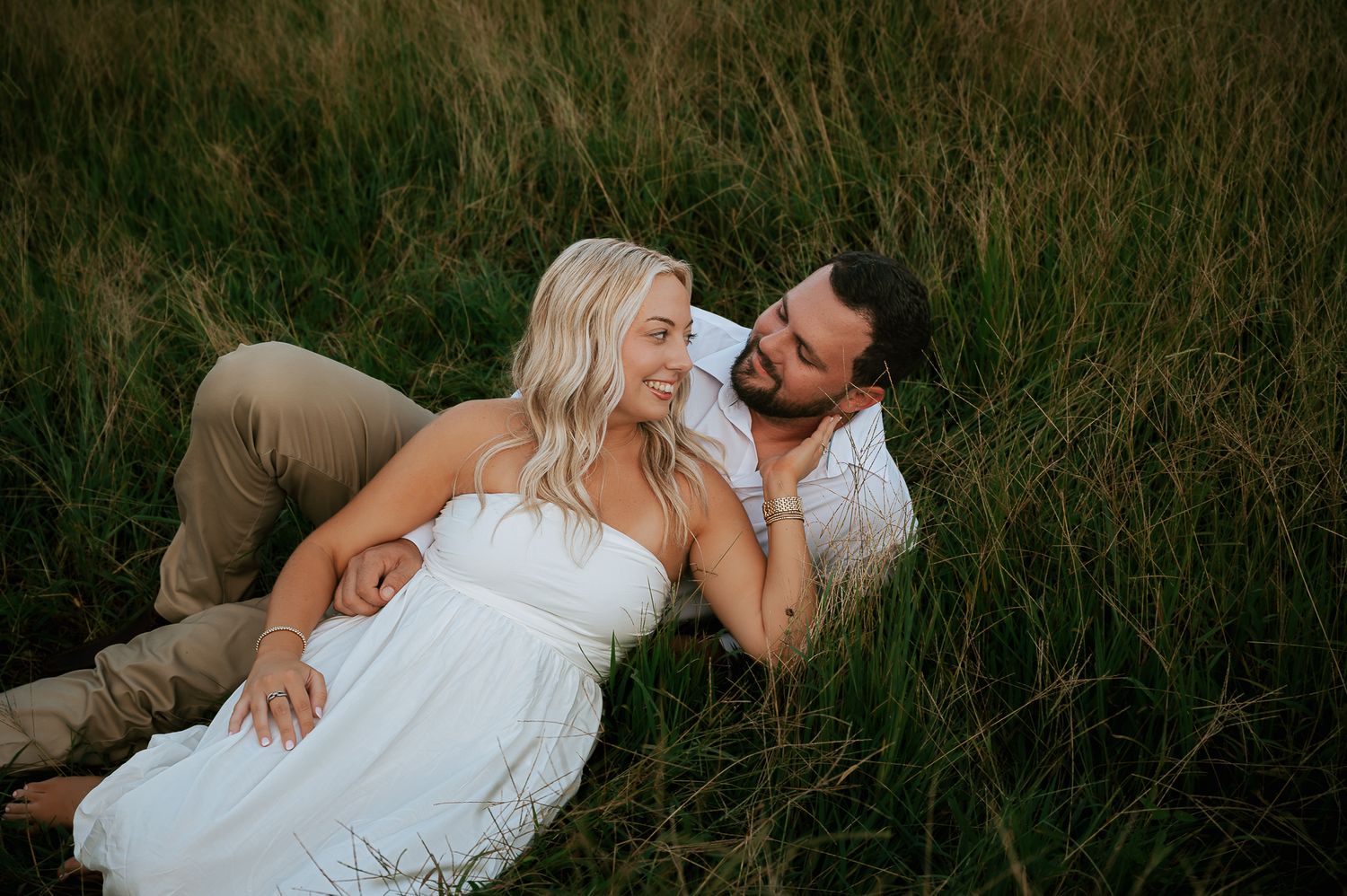 Romantic couple lying in tall grass field during golden hour photo session.