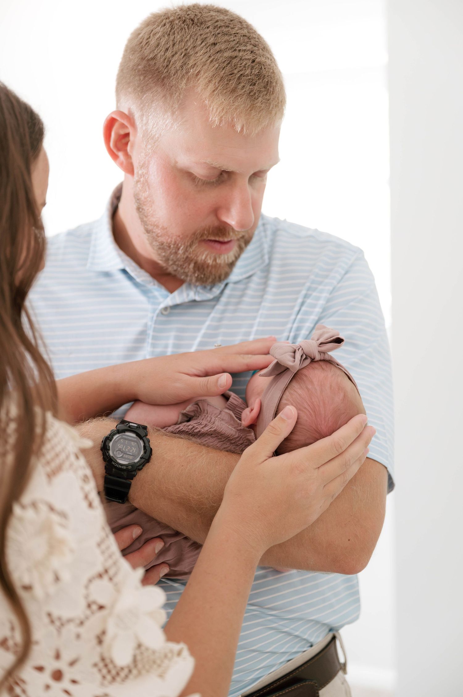 New parents tenderly hold their swaddled newborn baby, father in blue striped shirt gazing lovingly at infant.