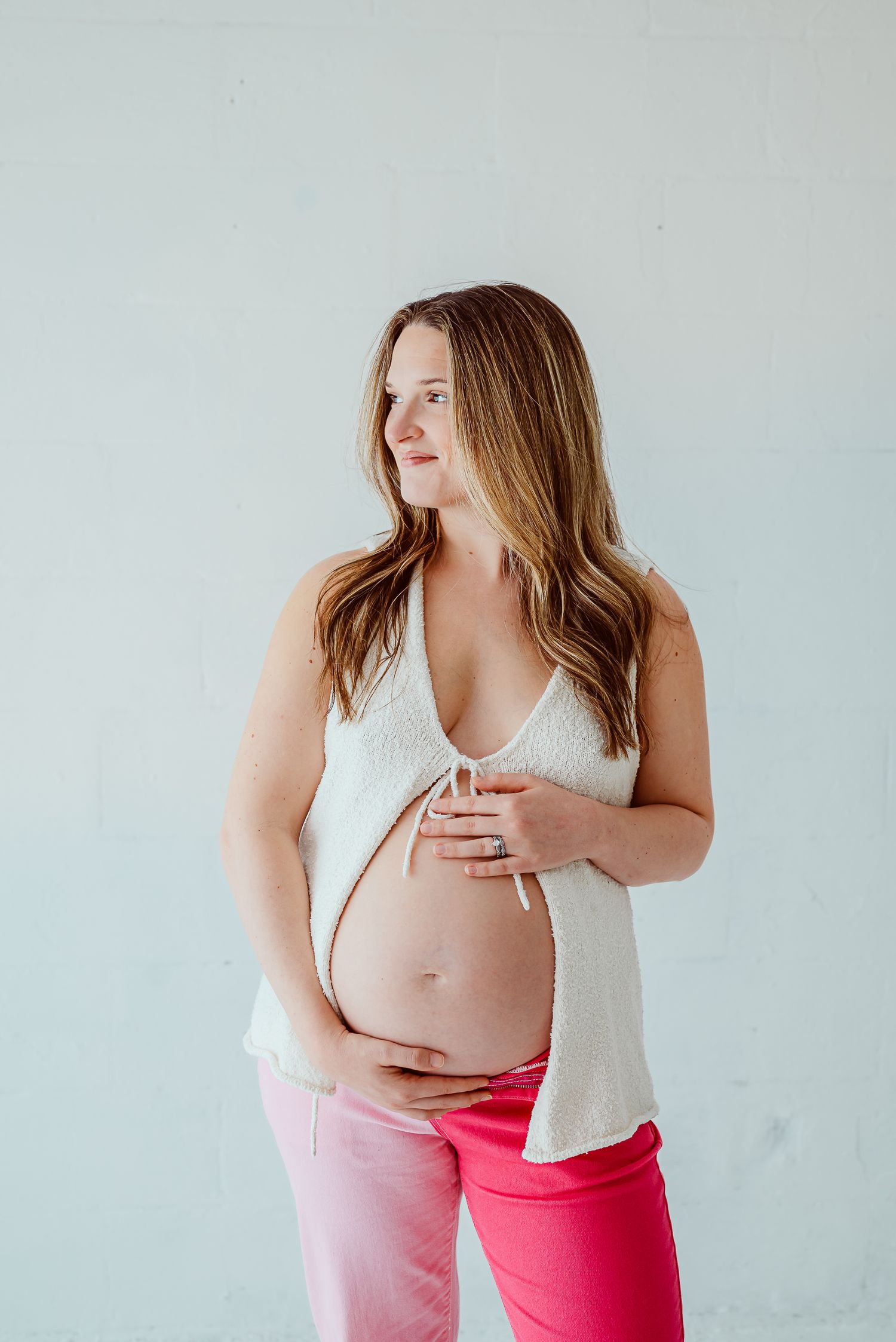 Maternity portrait in neutral tones showing pregnant belly against light background.