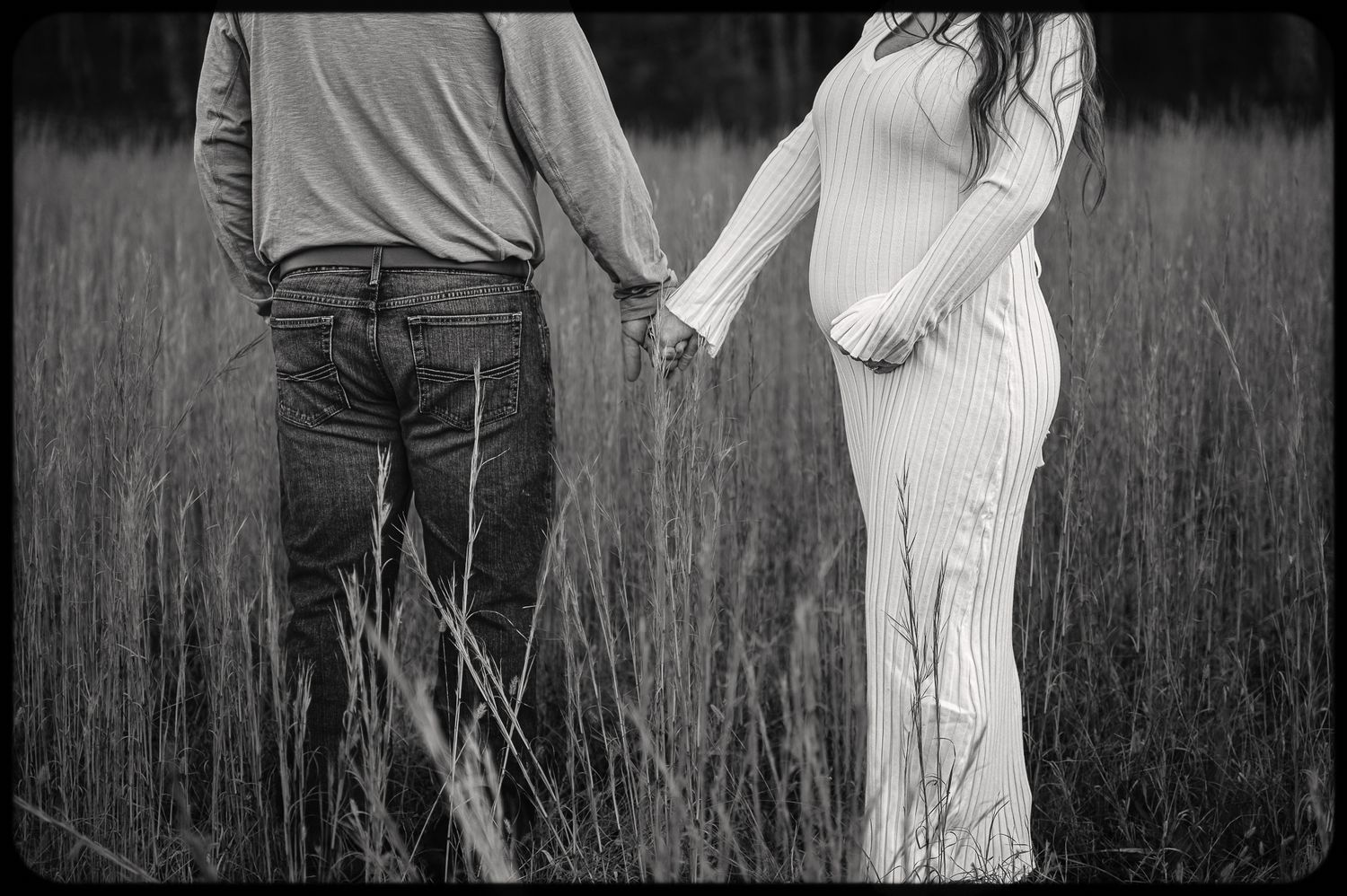 A couple embraces in a field of tall grass at sunset wearing black and white outfits.