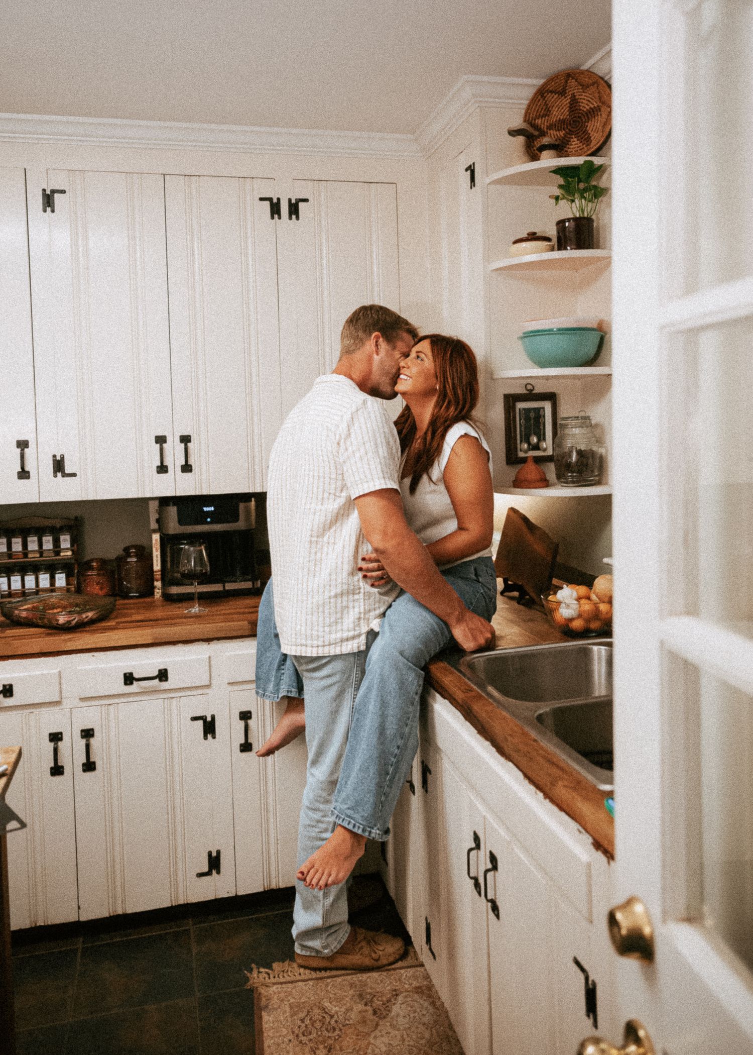 An intimate kitchen scene with white cabinets and wooden countertops in warm lighting.