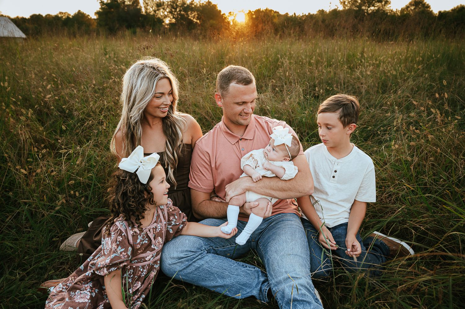 A loving family photoshoot in a golden field at sunset with warm lighting and natural poses.