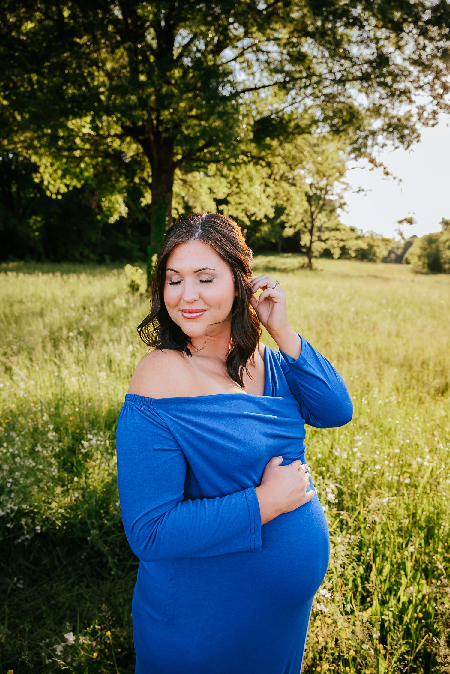 Woman in royal blue off-shoulder top poses gracefully in a sunlit meadow with wildflowers.