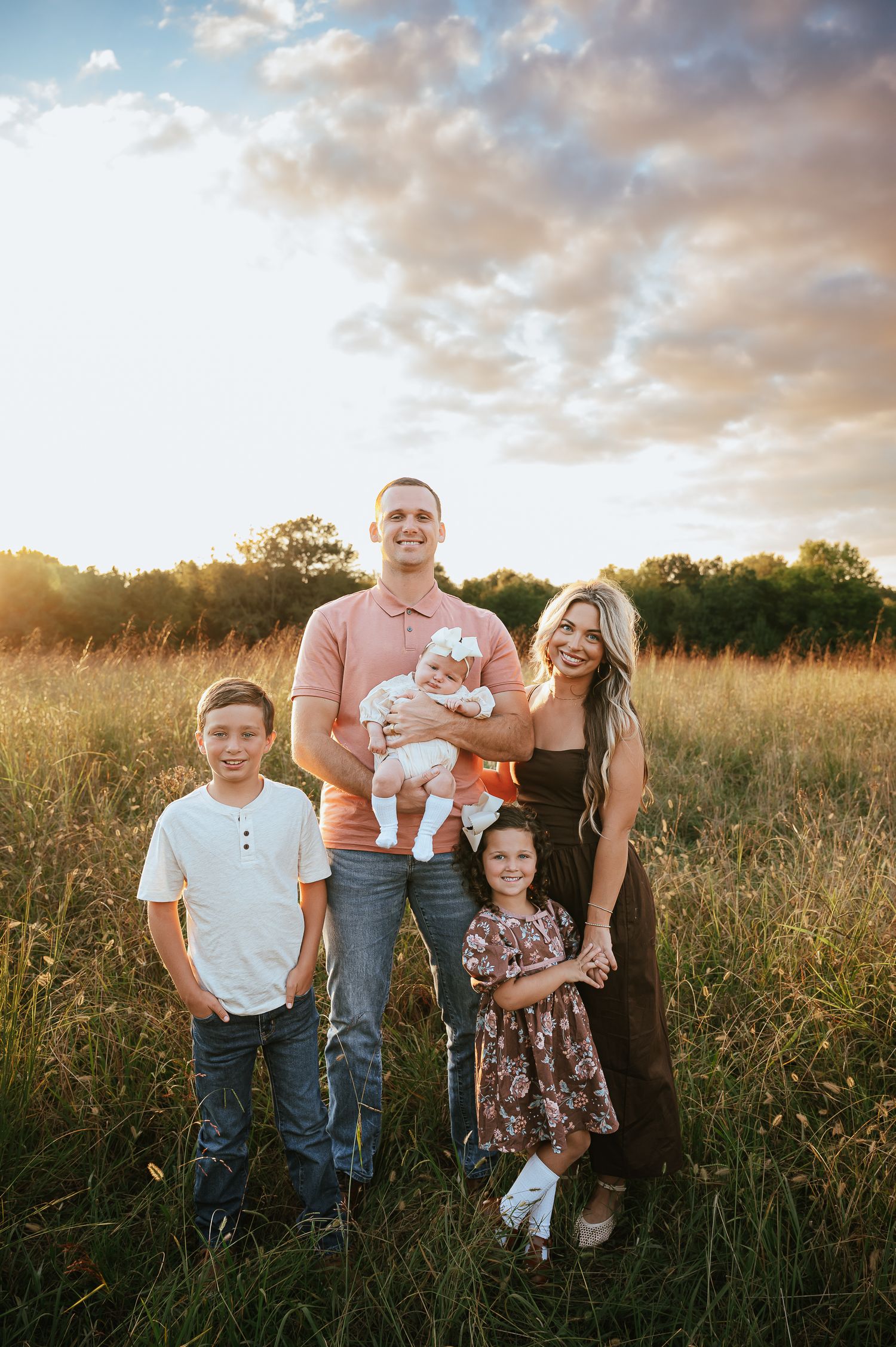 A family portrait in a golden field at sunset with a cloudy sky backdrop.