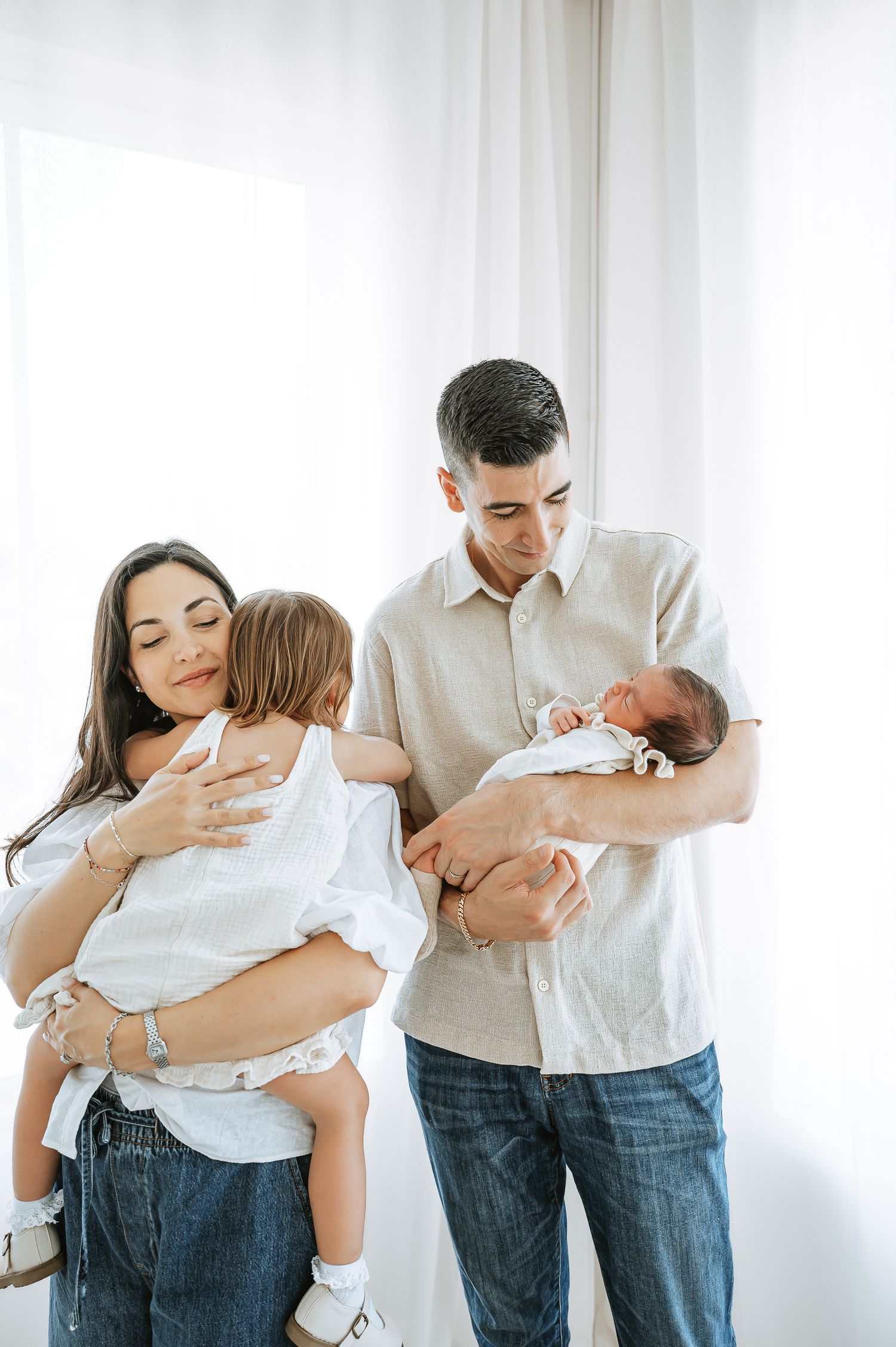 A family portrait in white clothing against a bright window backdrop.