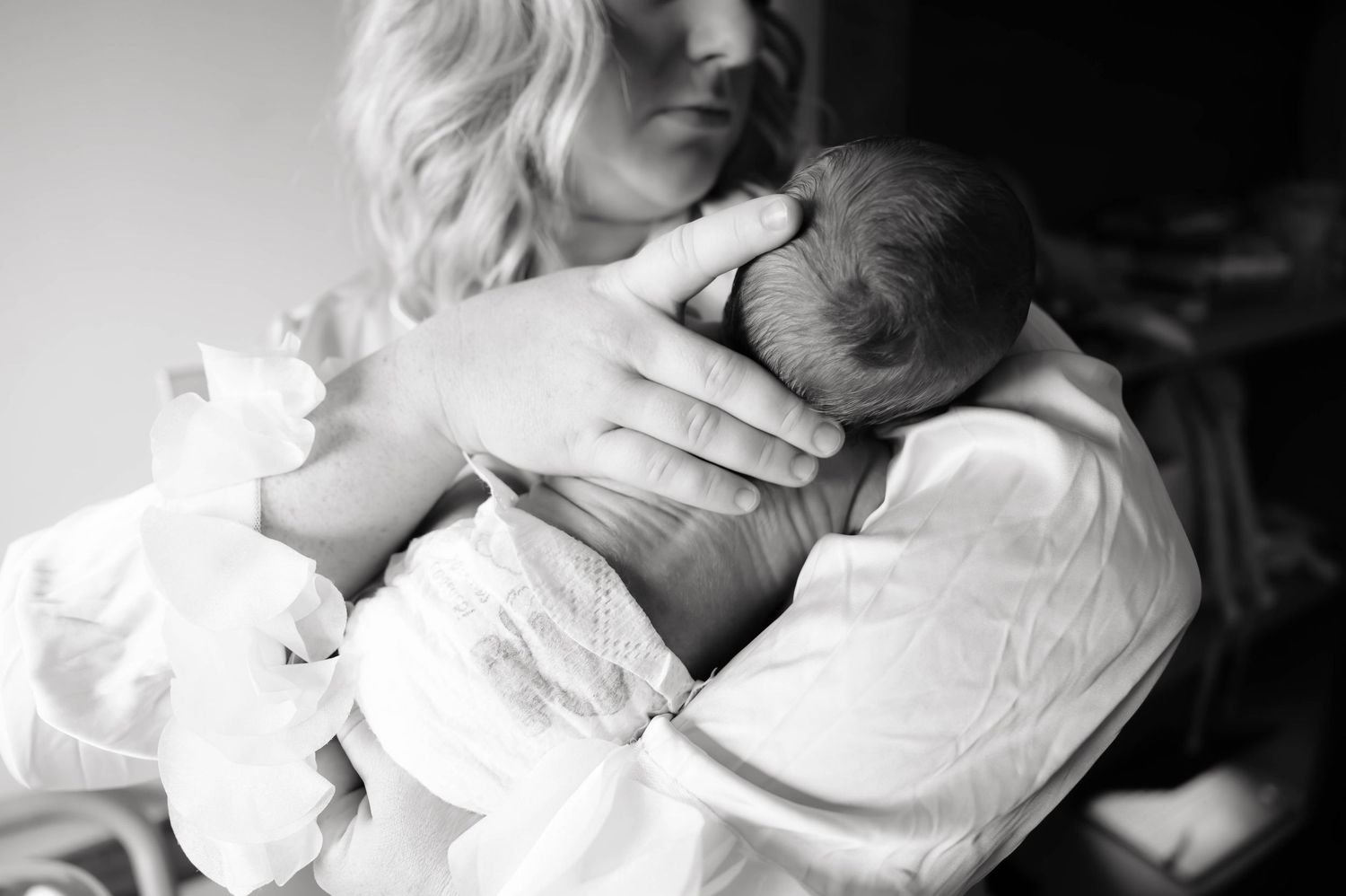 Black and white photo of a mother tenderly cradling her newborn baby close to her chest.