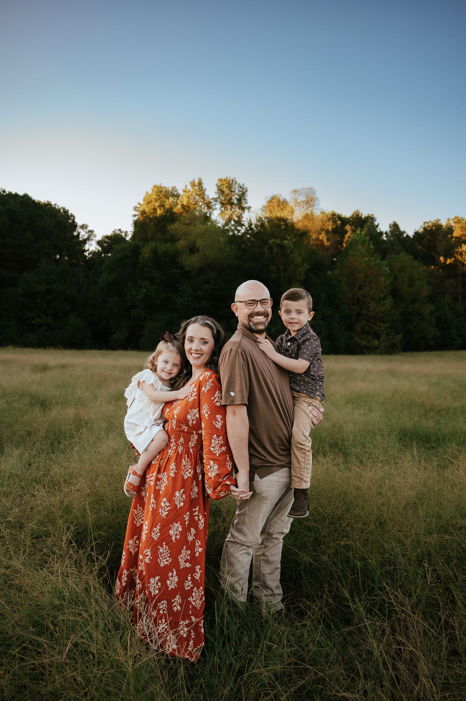 Family poses together in field during sunset portrait session.