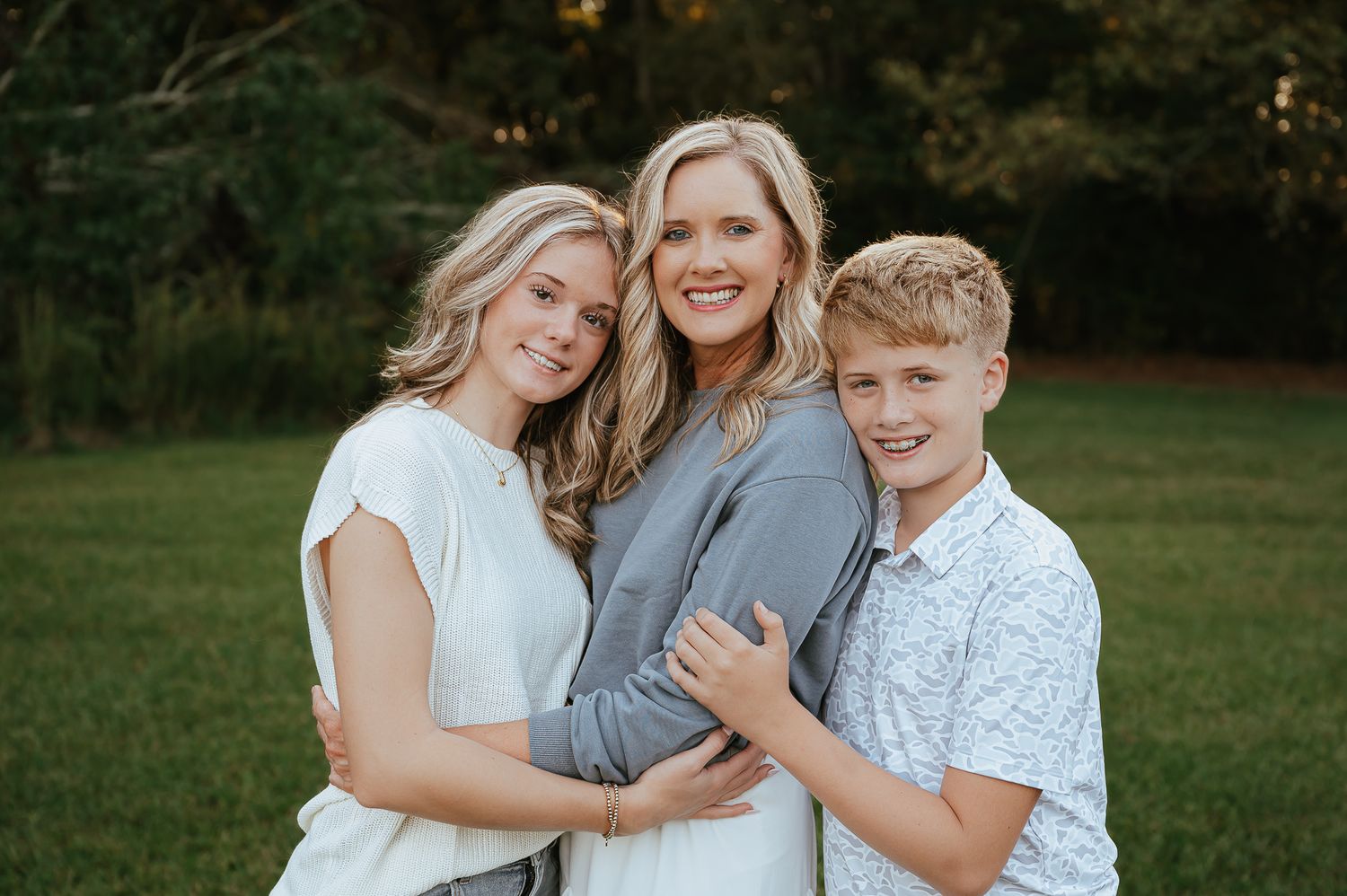 Three people embrace while smiling during outdoor maternity photo session.
