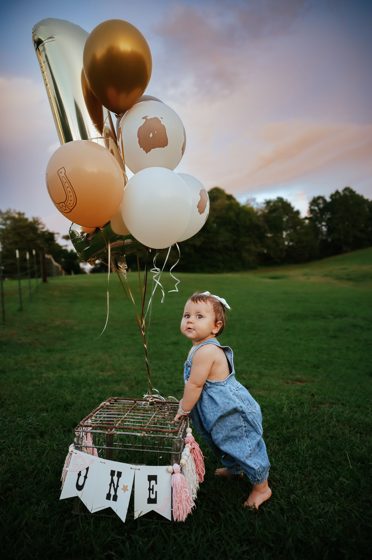 Child in overalls next to balloons and decorative box at sunset.
