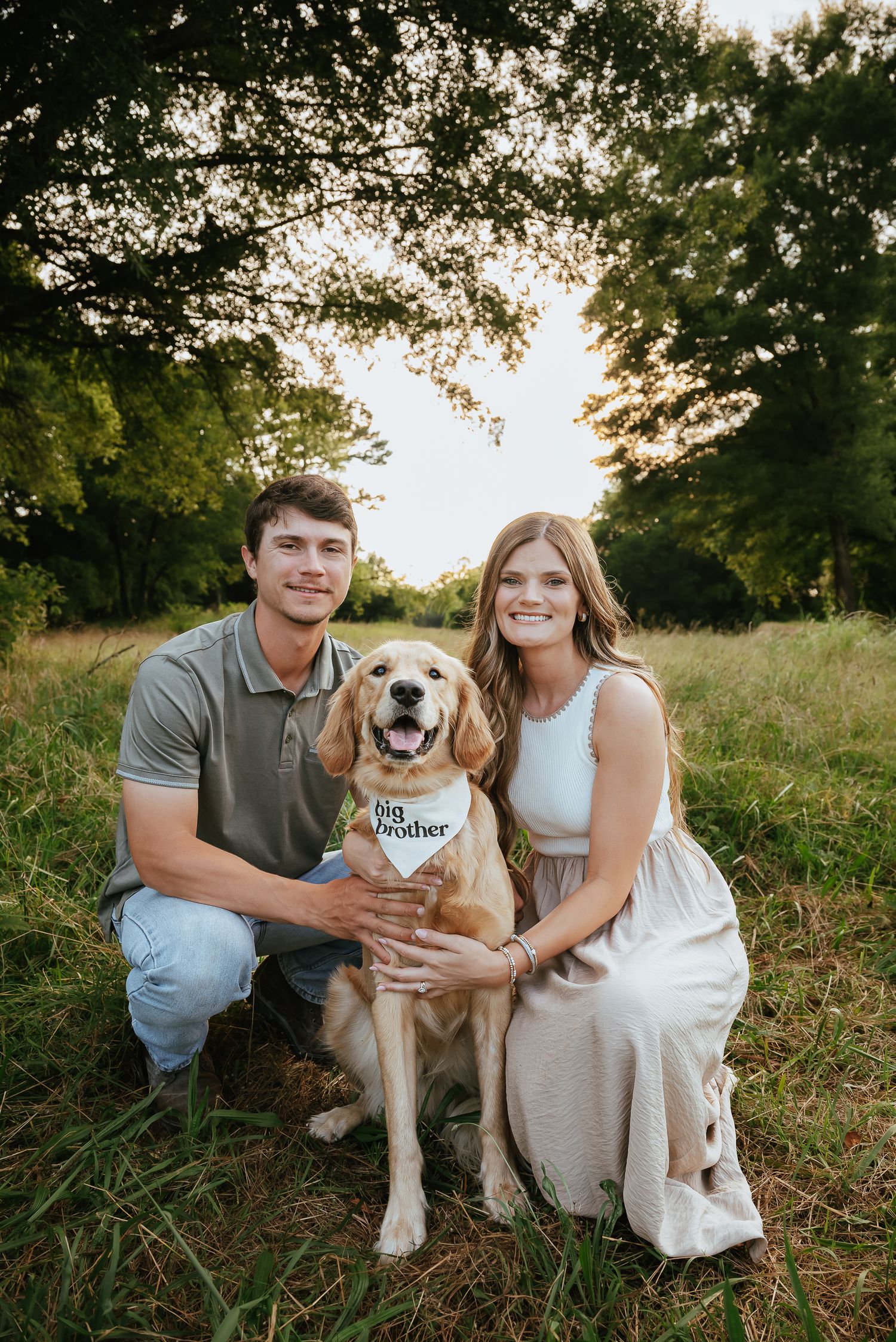 Family portrait in a grassy field with their golden retriever wearing a bandana.