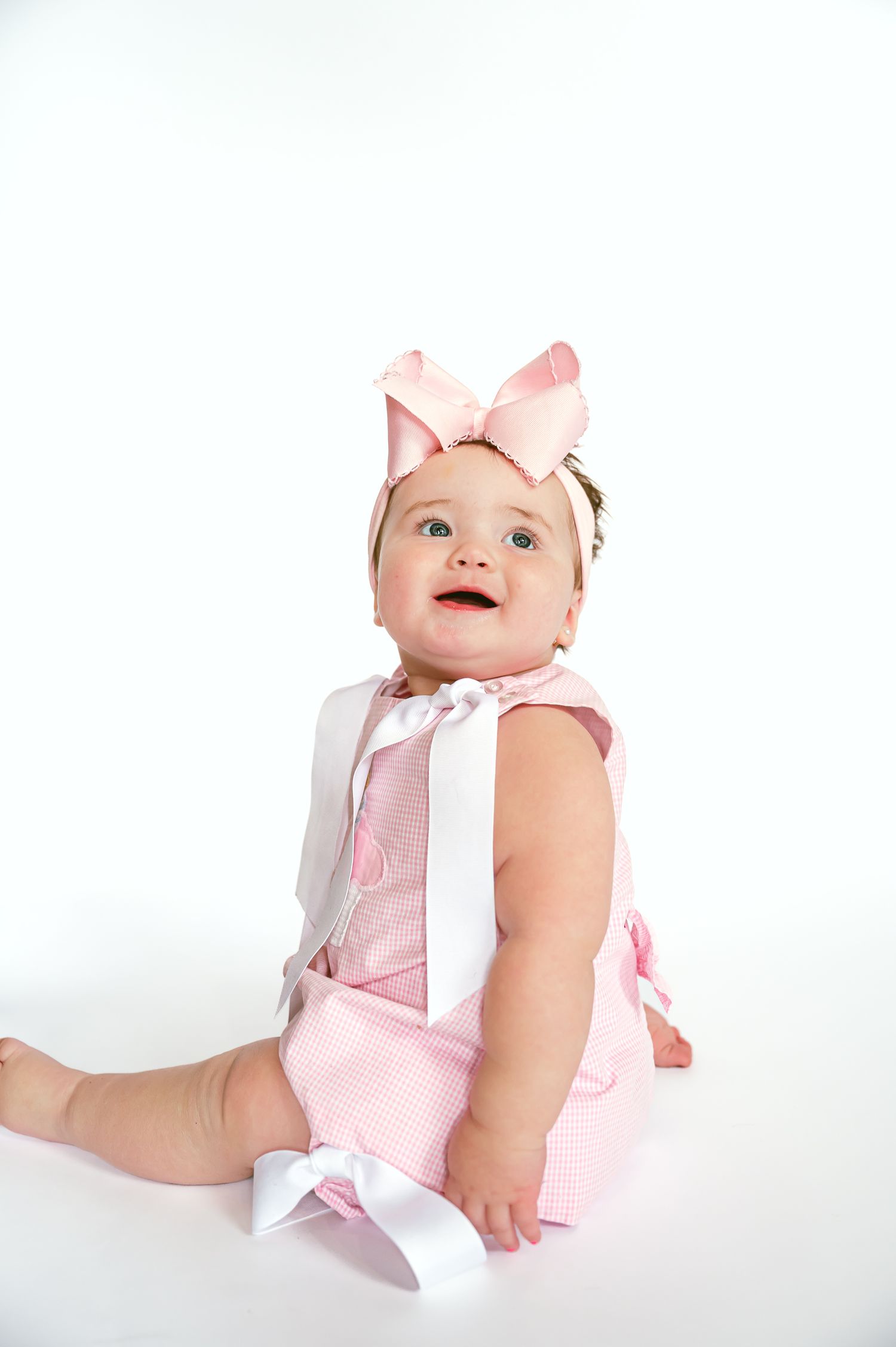 Baby wearing pink outfit sitting against white background.