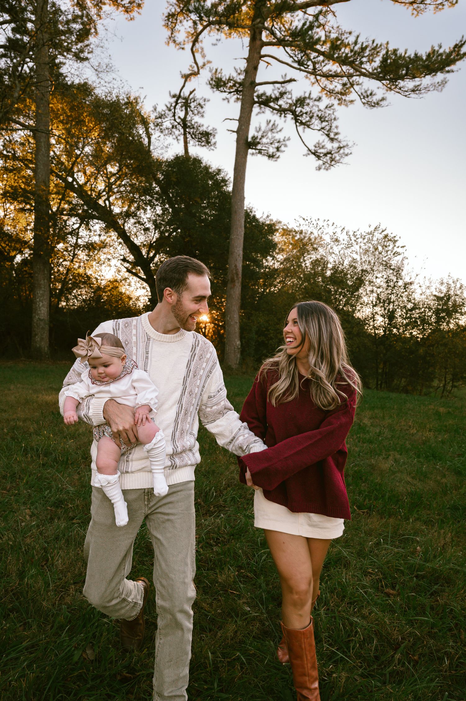 A family enjoying an autumn sunset together in a grassy field with tall trees in the background.