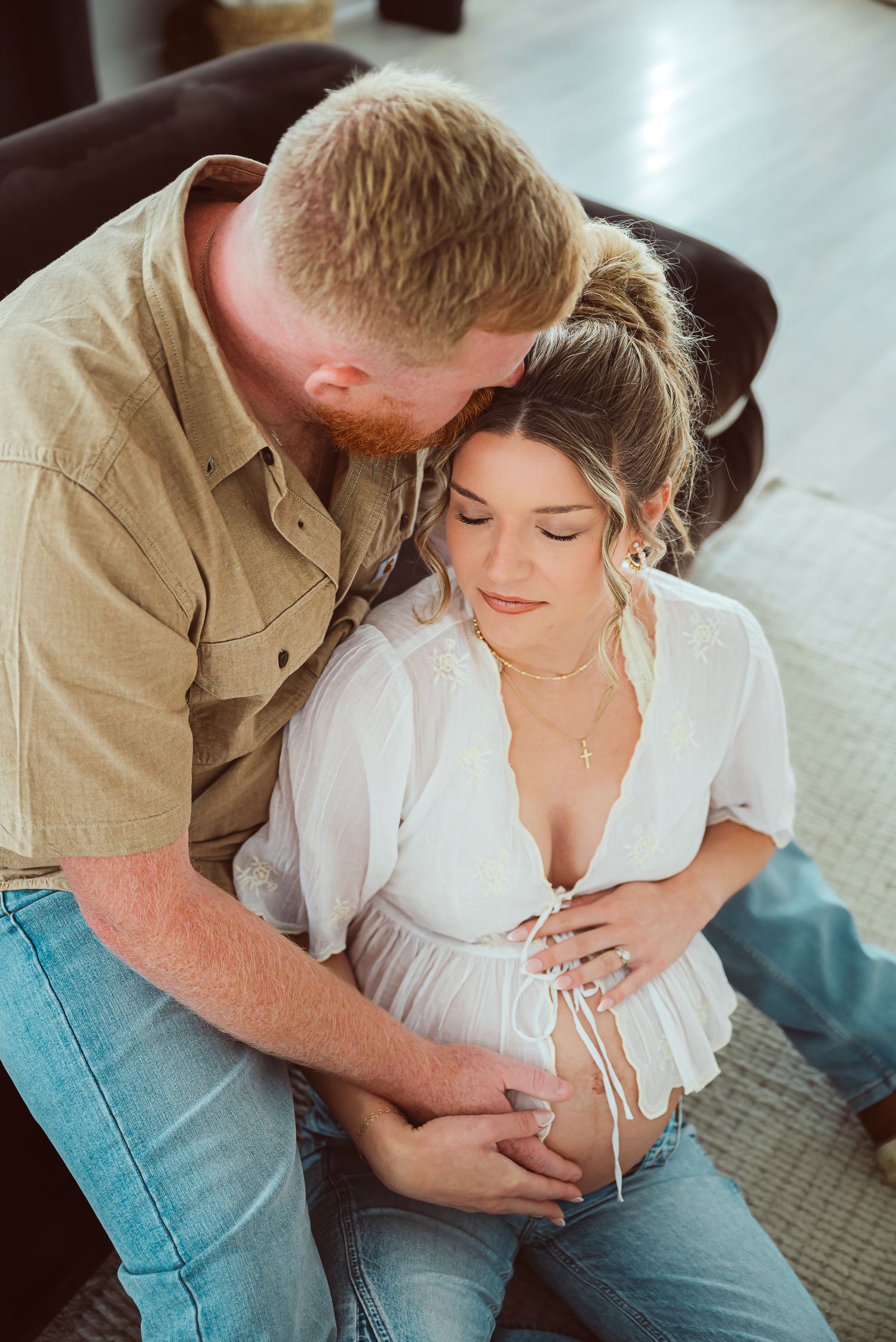 Intimate couple moment captured on floor with soft natural lighting.
