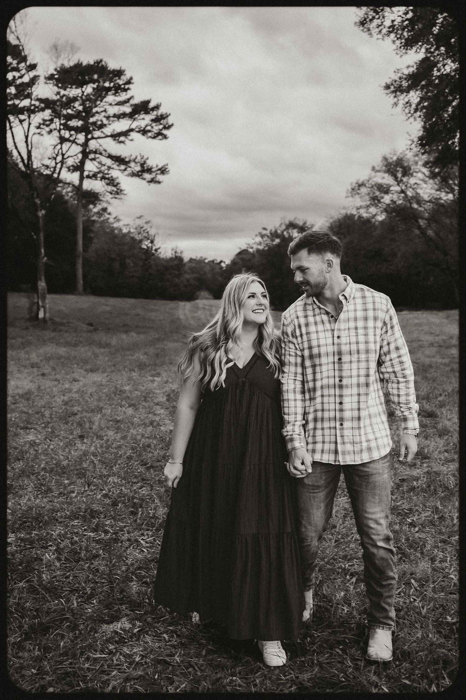 Black and white portrait of couple walking together in a rustic field setting.