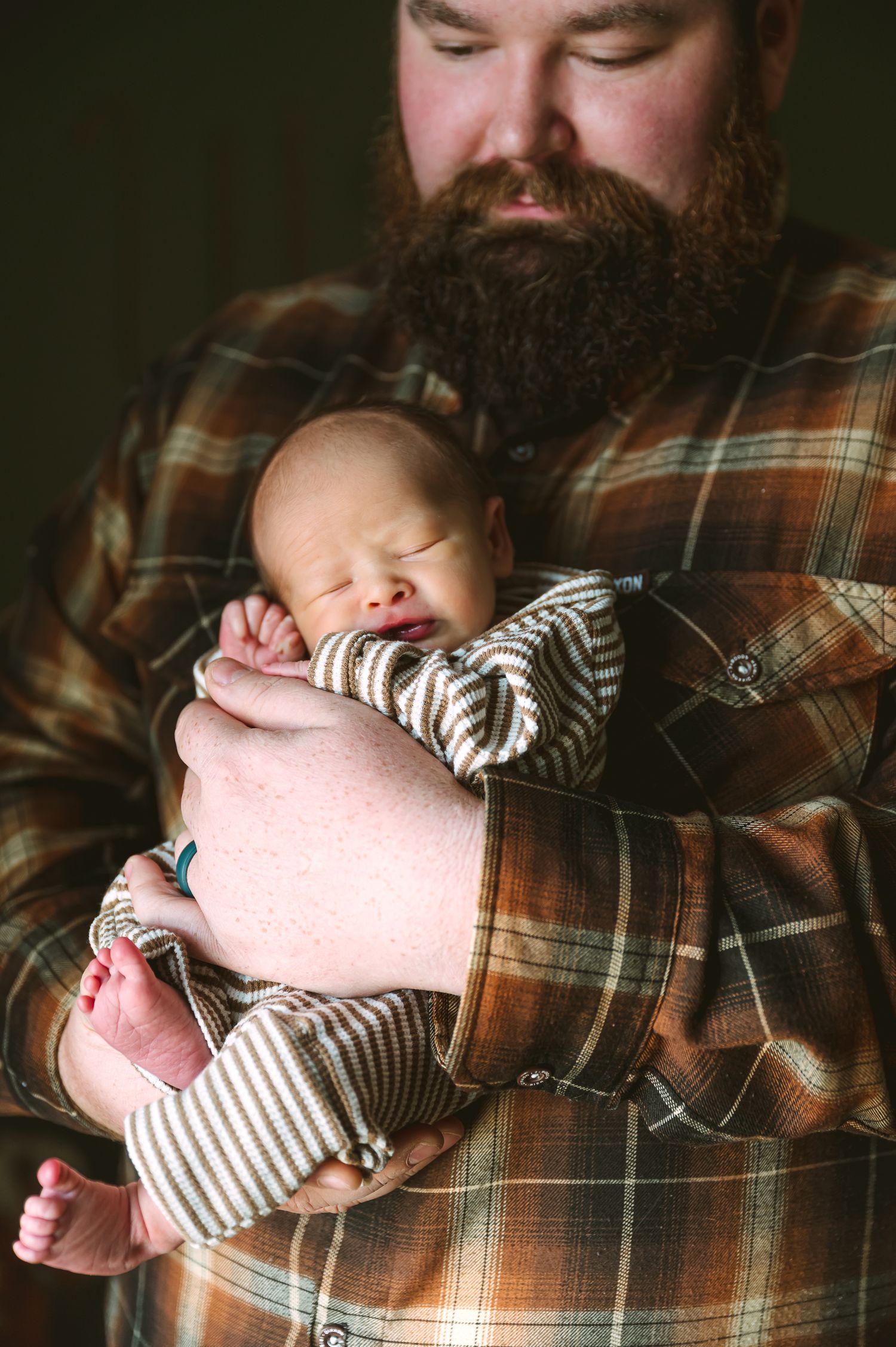 Baby sleeps peacefully in striped onesie while being held in plaid flannel.