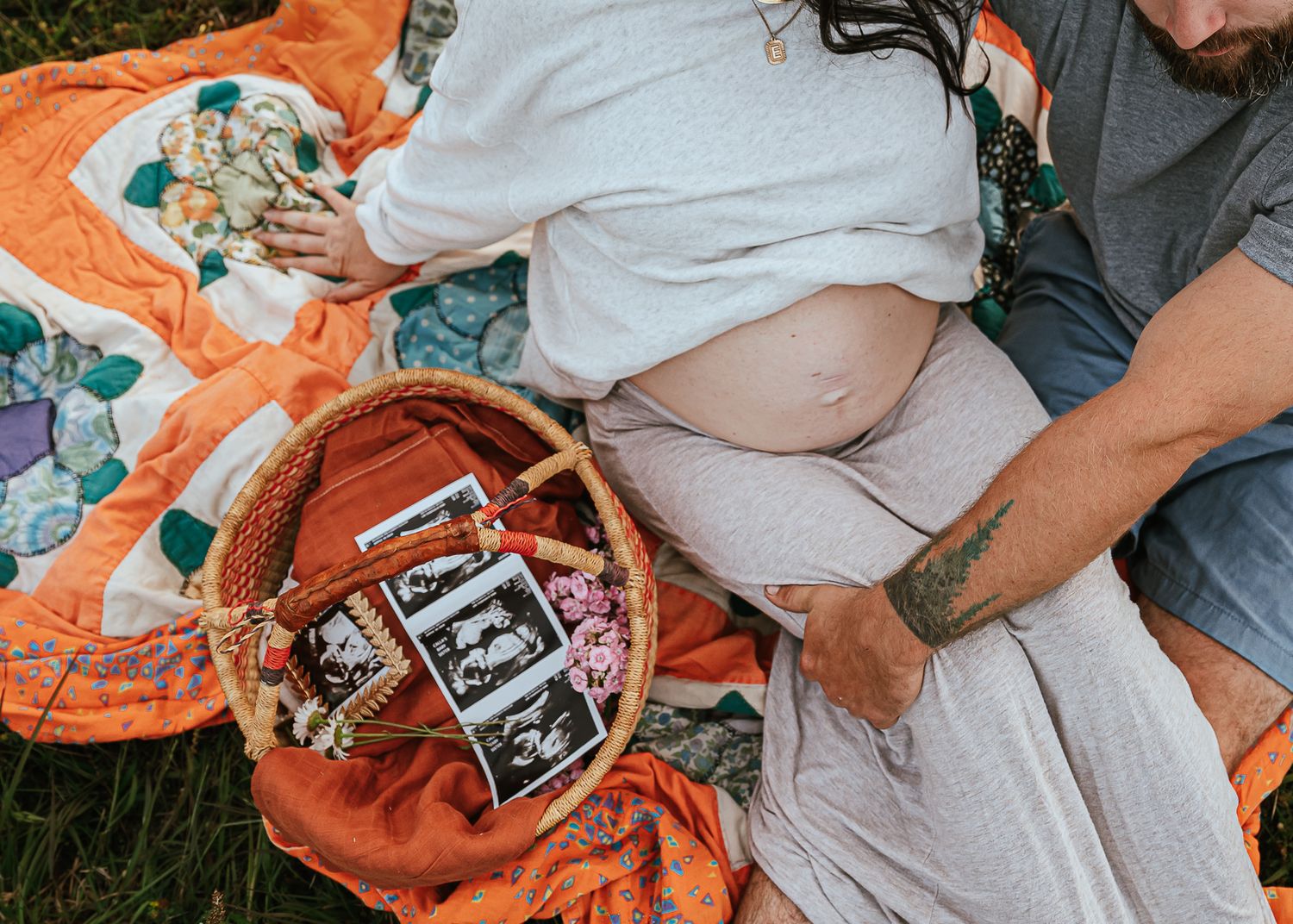Pregnancy announcement setup with ultrasound photos on orange blanket outdoors.
