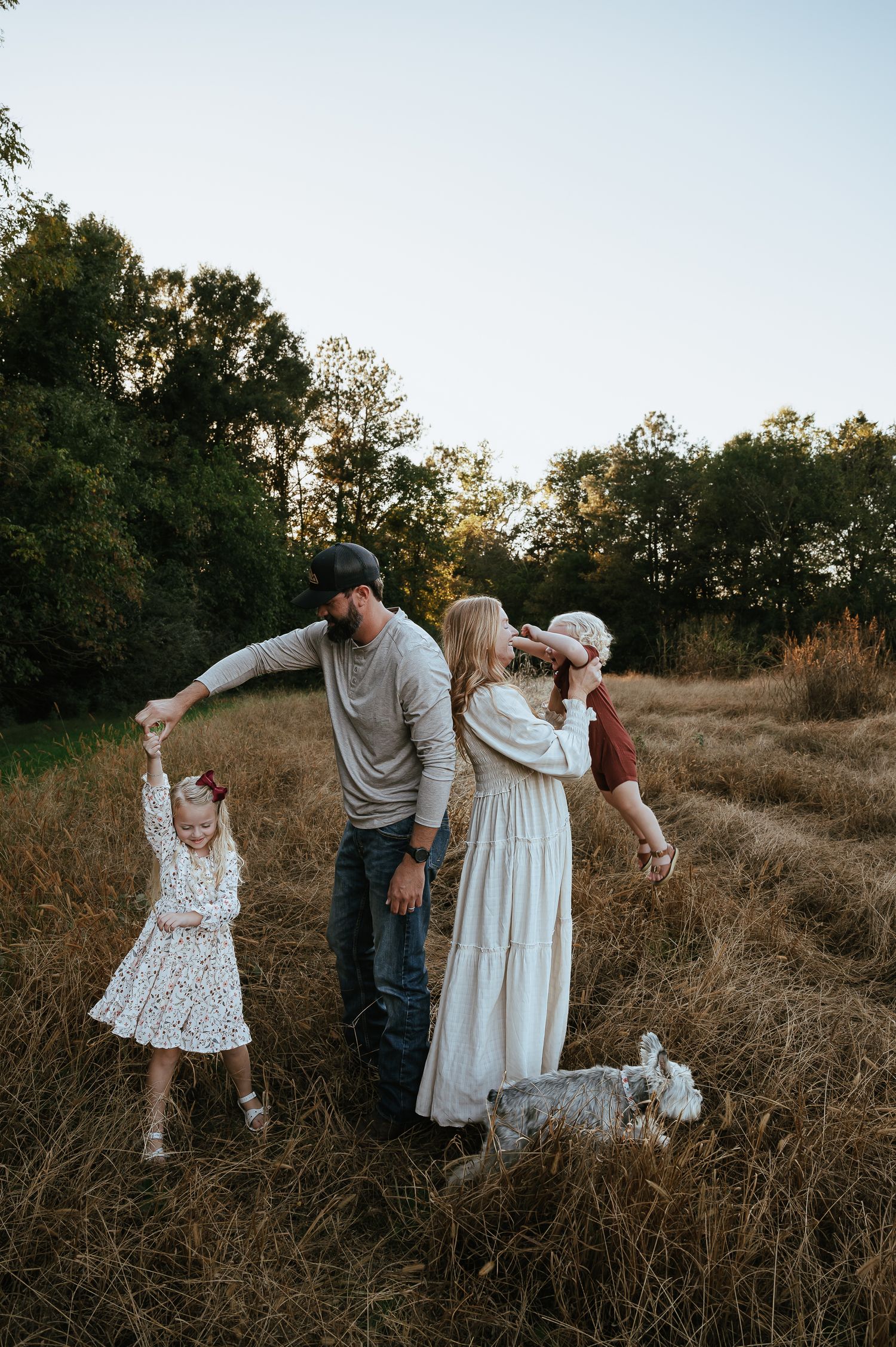 Family walks through tall grass field during golden hour photo session.