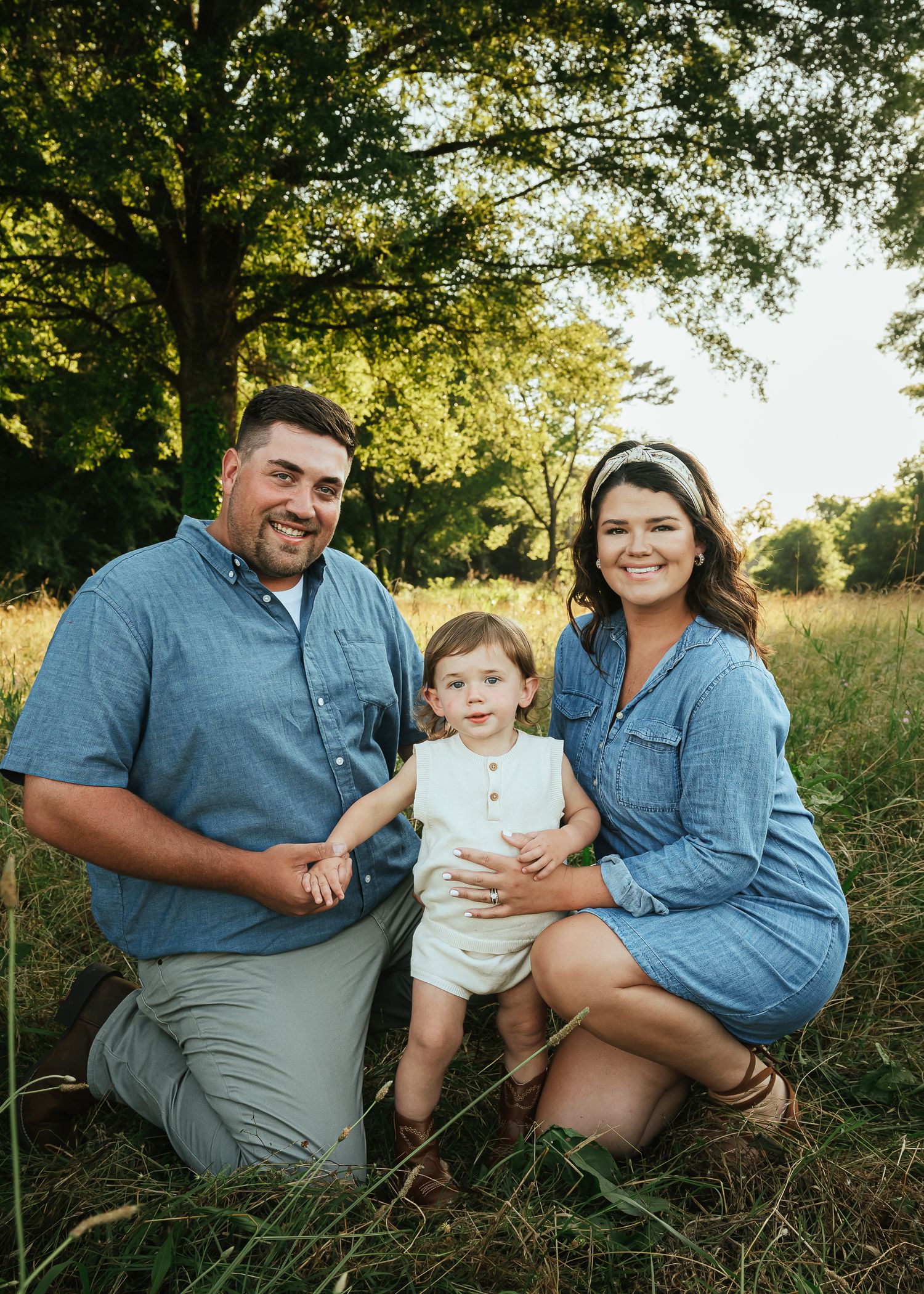 Family wearing coordinated blue outfits sitting together in a grassy field at golden hour.