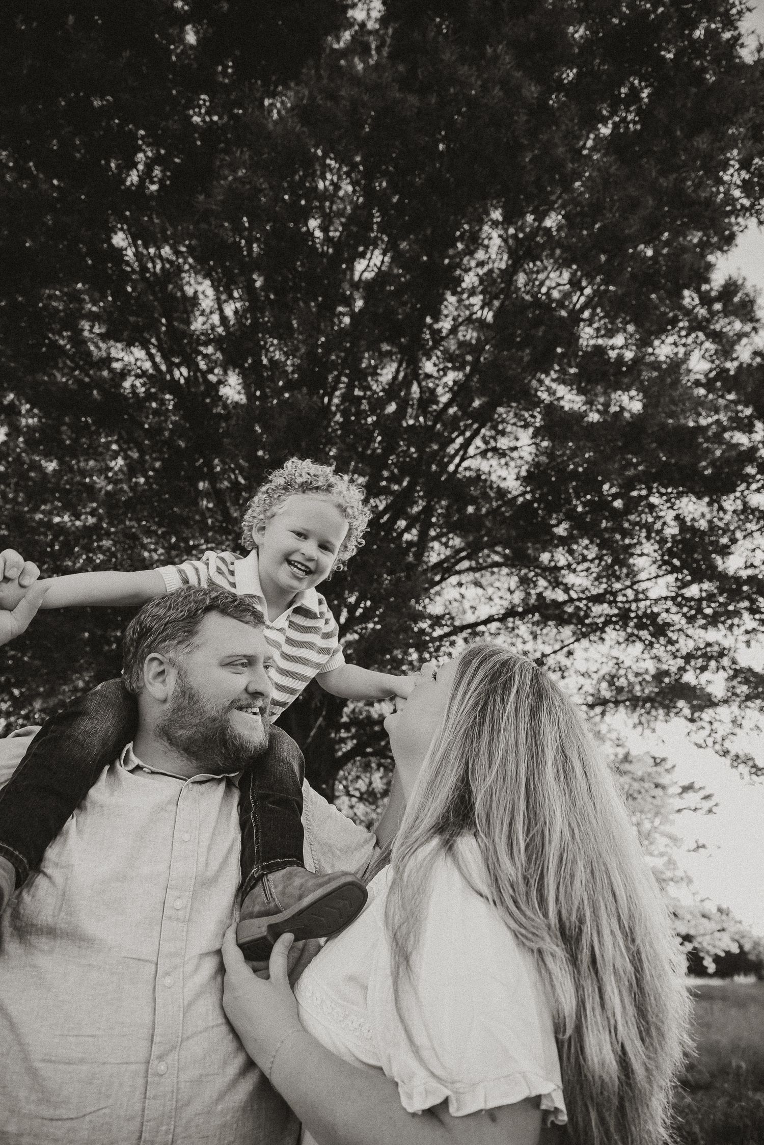 Black and white candid family moments captured under tree canopy.