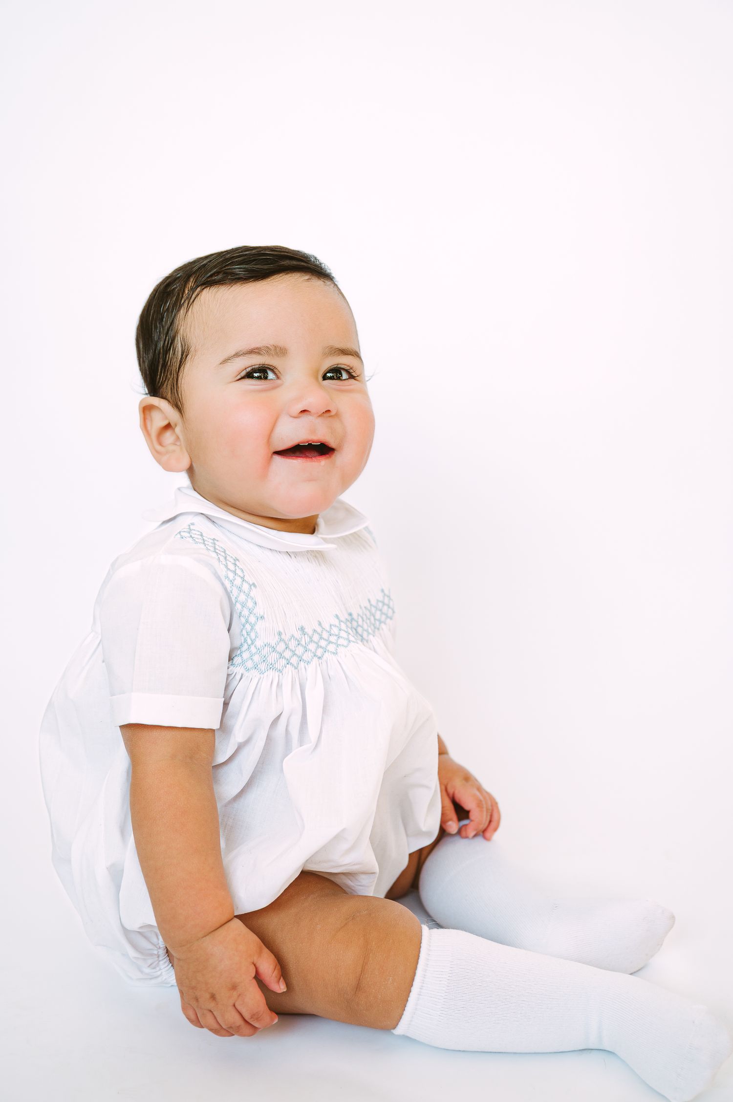 Baby in white clothing photographed against clean white background.