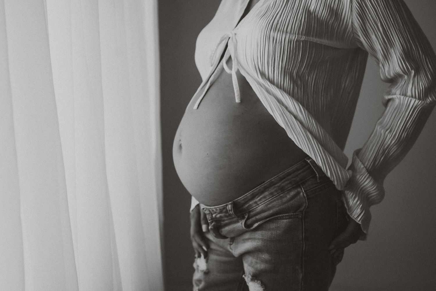 Black and white artistic maternity photos showing a pregnant belly in dramatic lighting.