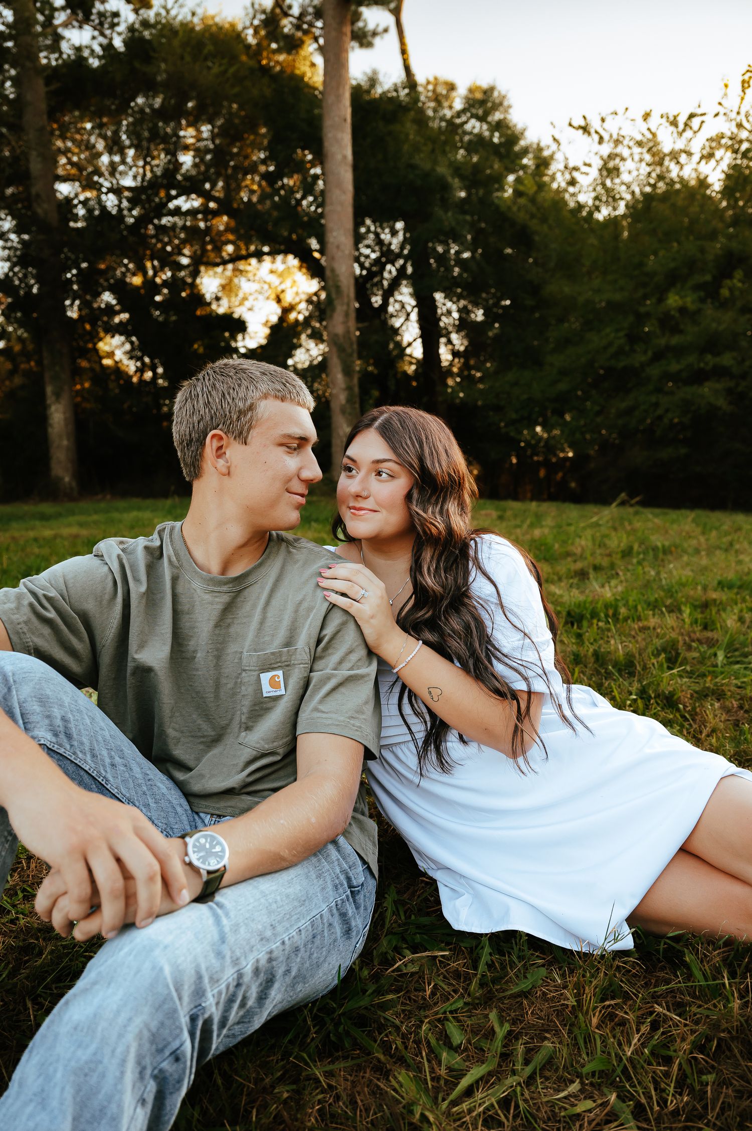 Couple lounging on grassy hillside during golden hour sunset photoshoot.