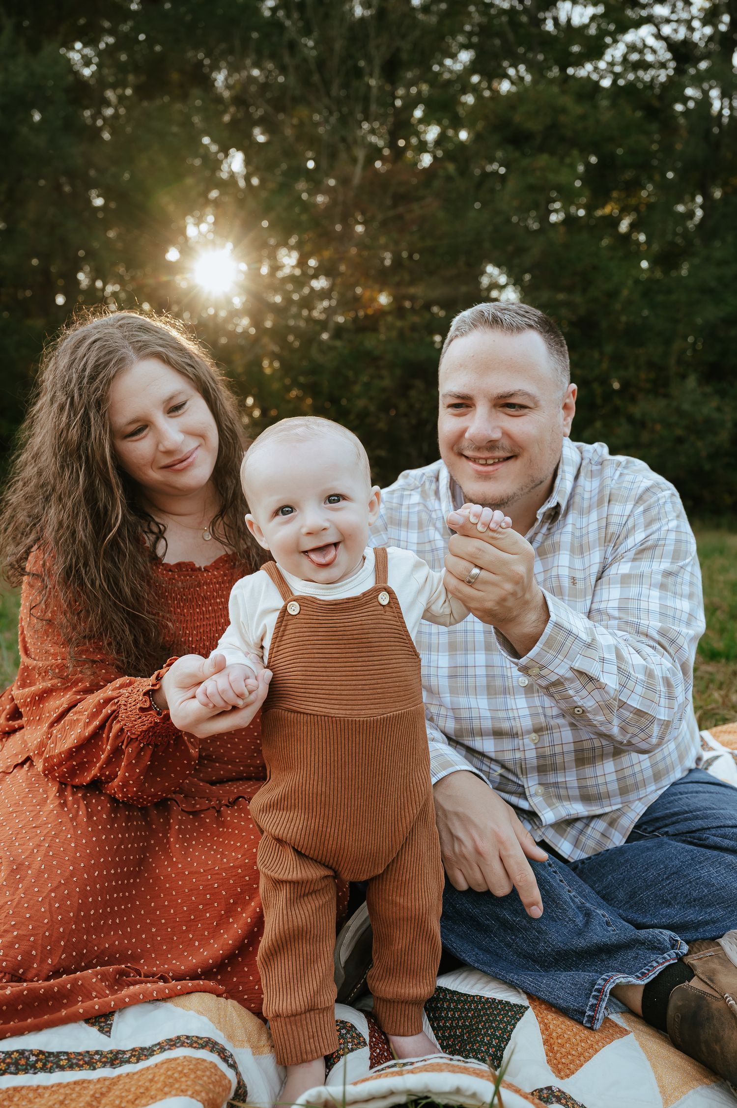 Family shares joyful moment on picnic blanket during sunset photo session.