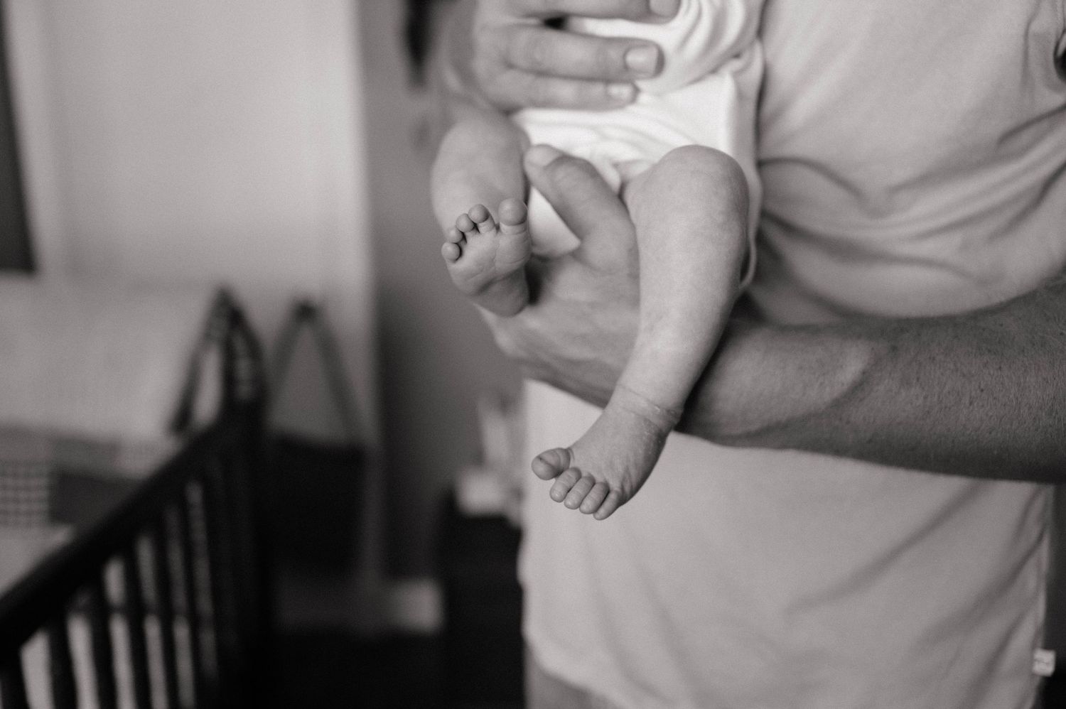 Black and white photo of a father cradling a newborn baby, focusing on tiny infant feet and hands.